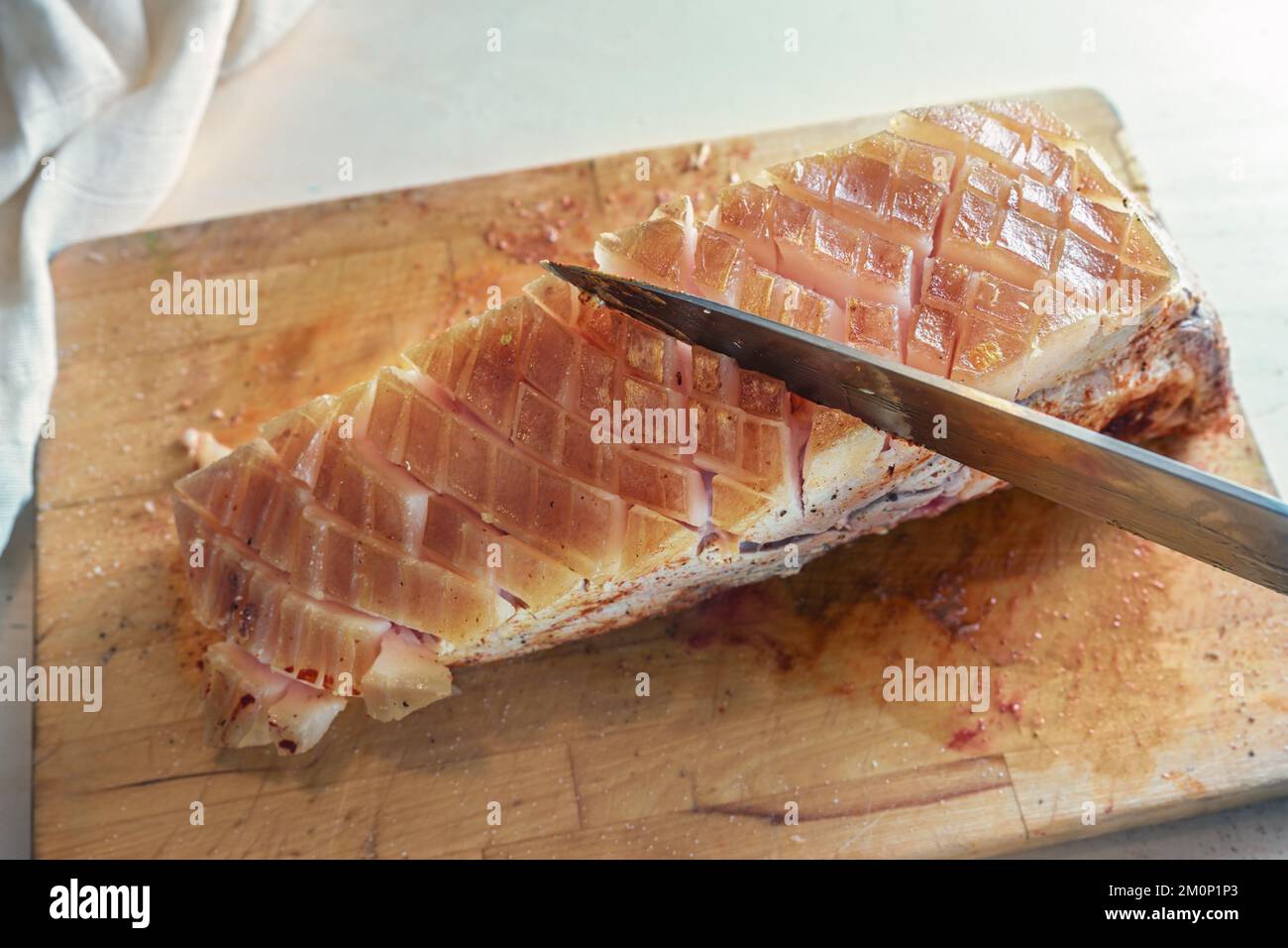 Fat rind of a piece of raw seasoned pork meat is incised with a kitchen knife on a cutting board, cooking preparation for a delicious crust roast, sel Stock Photo