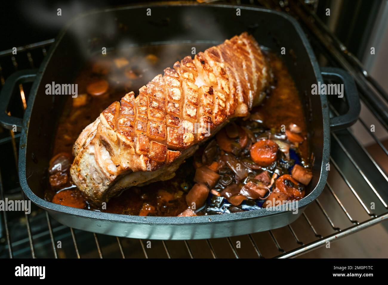 Festive crust roast from pork meat with crispy fat rind on a brown sauce base in a black cooking pan fresh from the oven, copy space, selected focus, Stock Photo