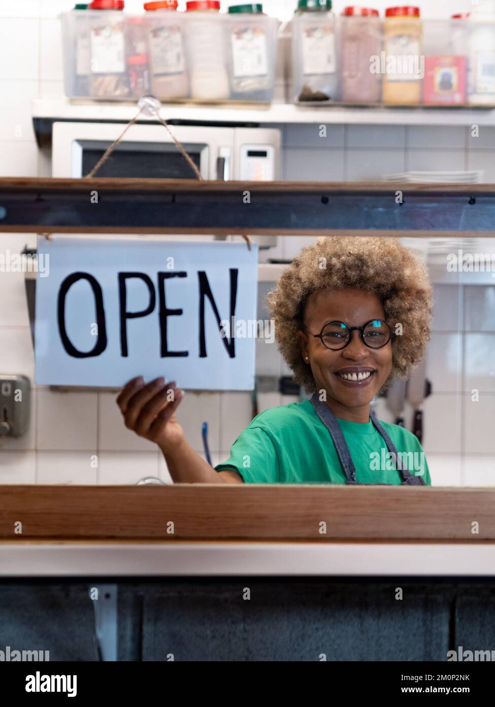 Happy African American woman looking at camera and Hanging Open Sign by the Glass Window Stock Photo