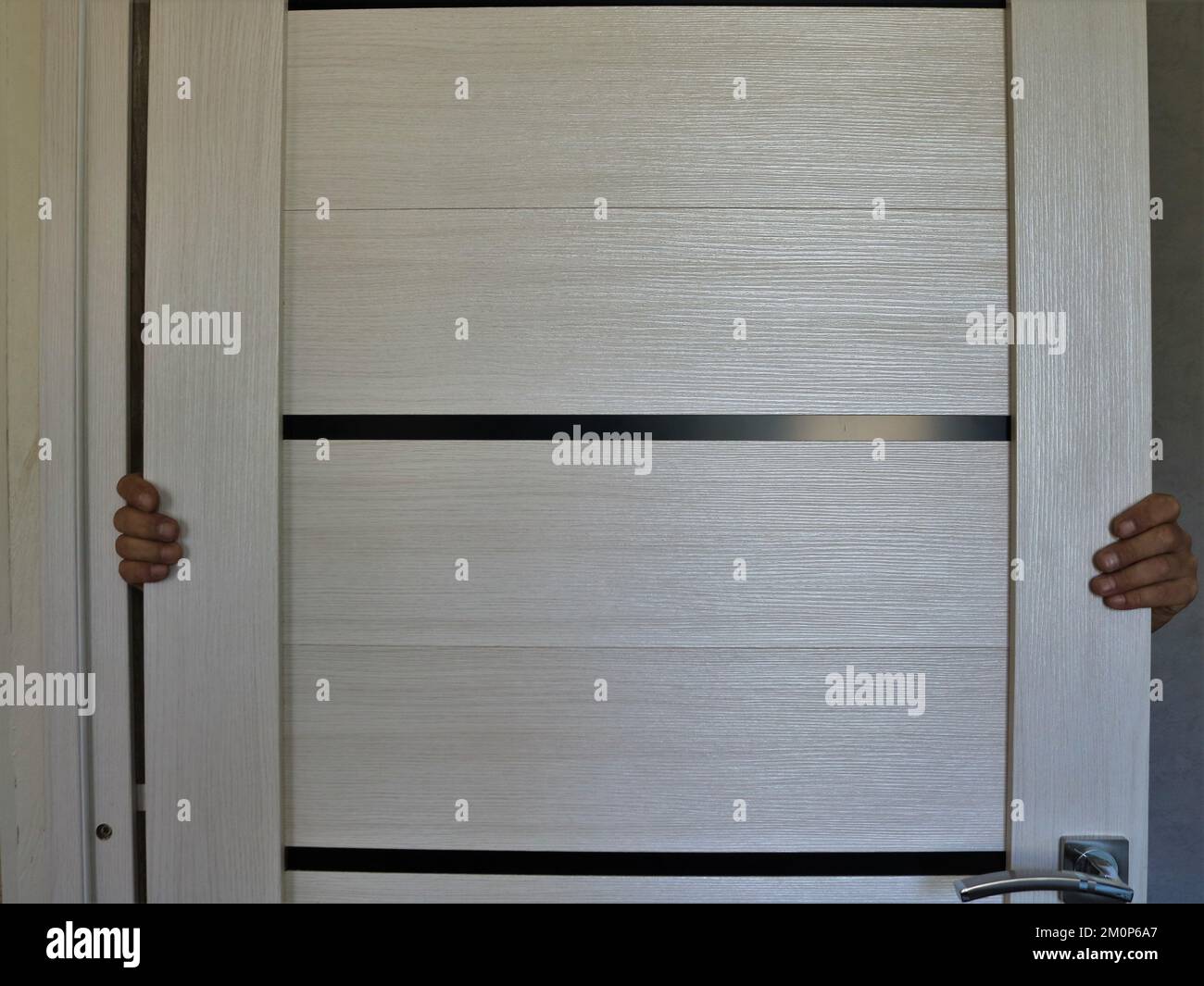 light leaf of a wooden room door and two hands holding it, a person