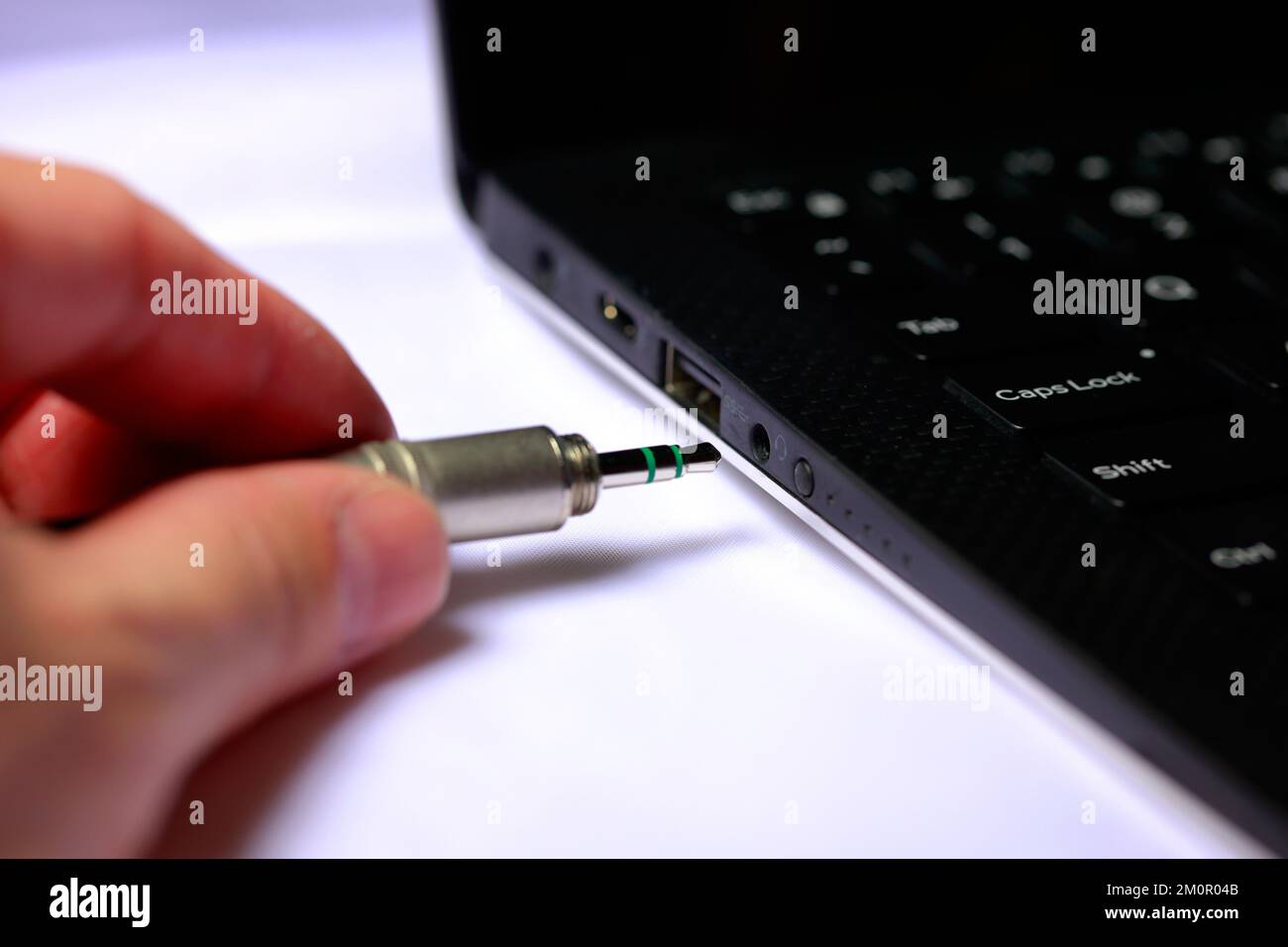 A person plugging a 3.5mm audio plug into a headphone jack on the side of a laptop. Stock Photo