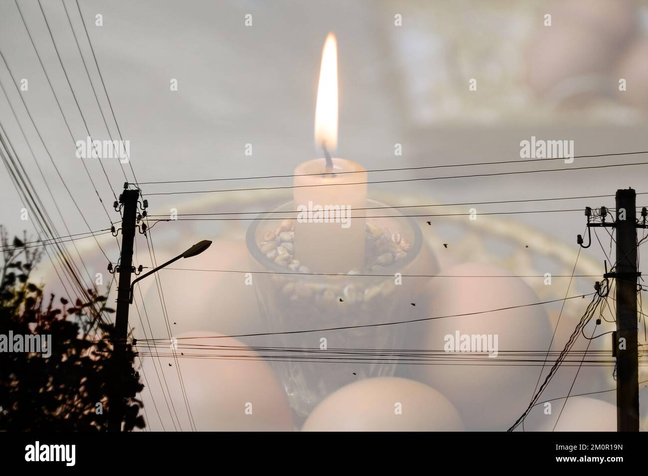 Blackout, power grid overloaded. Blackout concept. Earth hour. Burning flame candle and power lines on background. Energy crisis. Candle flame. Stock Photo