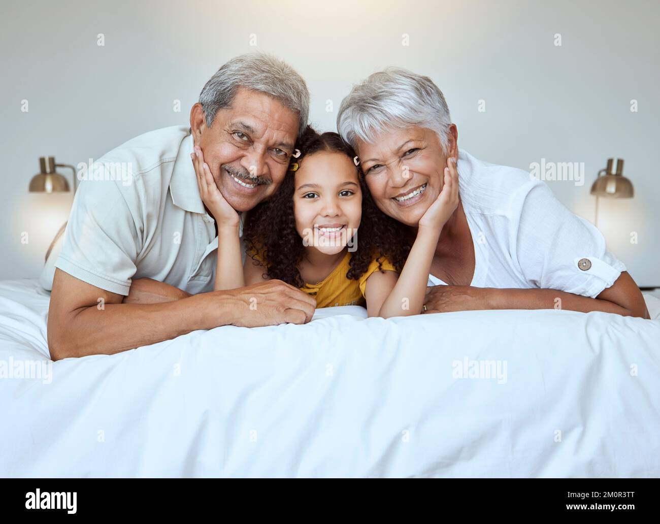 Girl, grandparents and smile on bed for portrait, together and bedroom for bonding, love and happy in home. Elderly, man and woman with child for Stock Photo