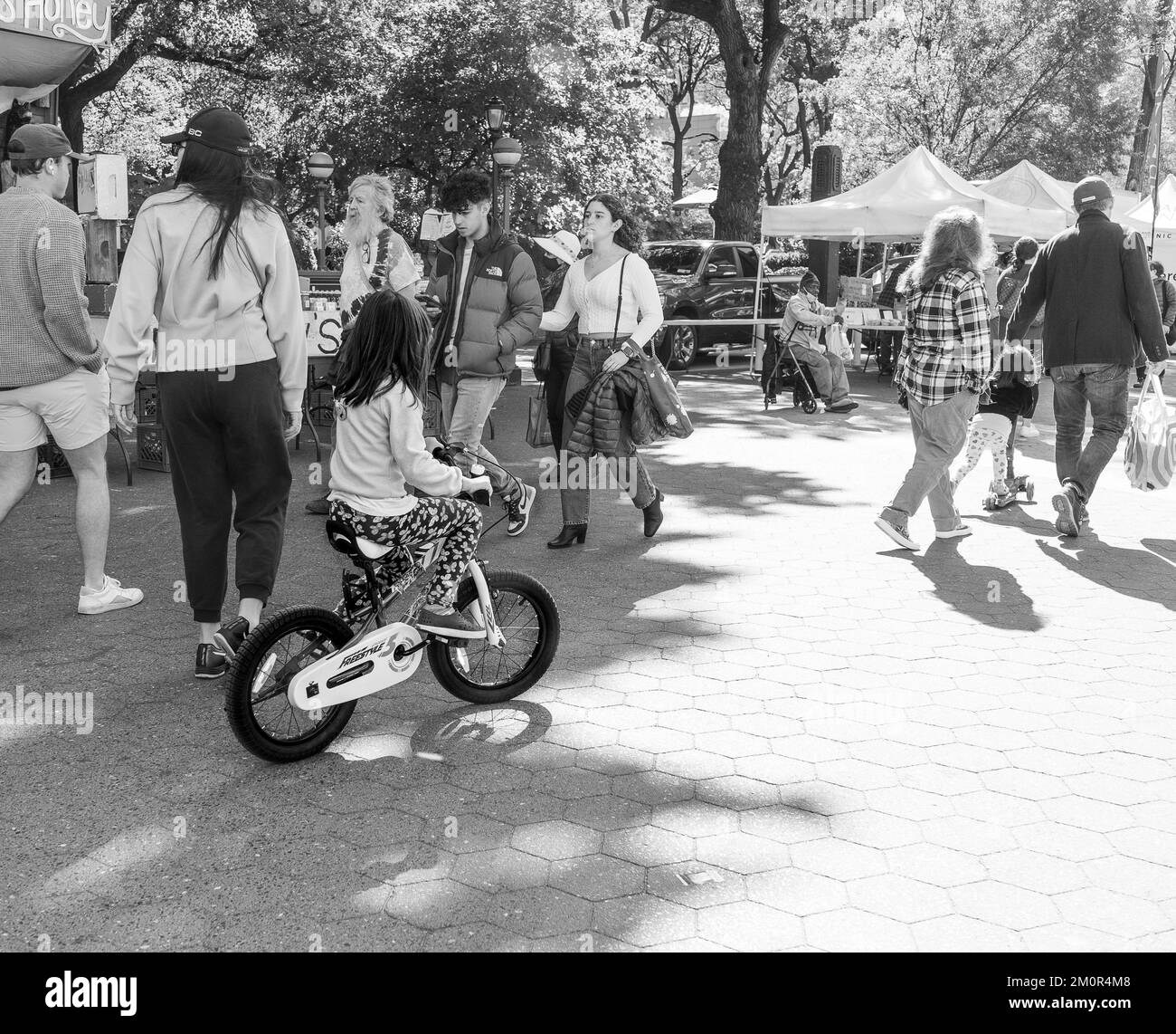 Little girl riding bicycle among people walking in the park in New York, black and white photography. Stock Photo