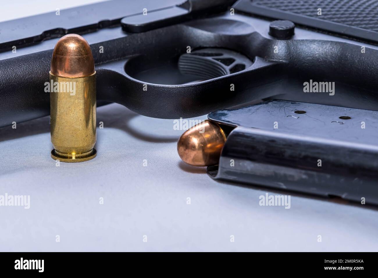 A black 45 caliber pistol a loaded magazine next it and an extra bullet on a white background Stock Photo