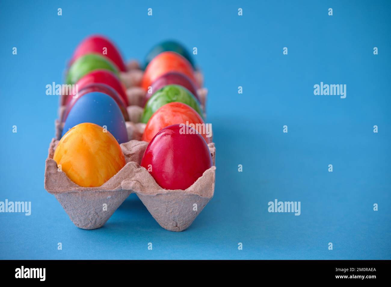 Colorful Easter eggs in cardboard box against blue background Stock Photo