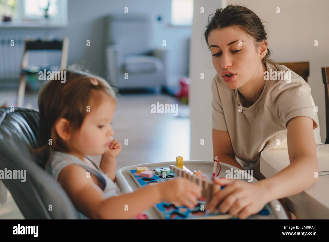 Happy little baby girl playing with colored wooden toy learning to count by playing with her mother at home. Teaching numbers at home. Childhood Stock Photo