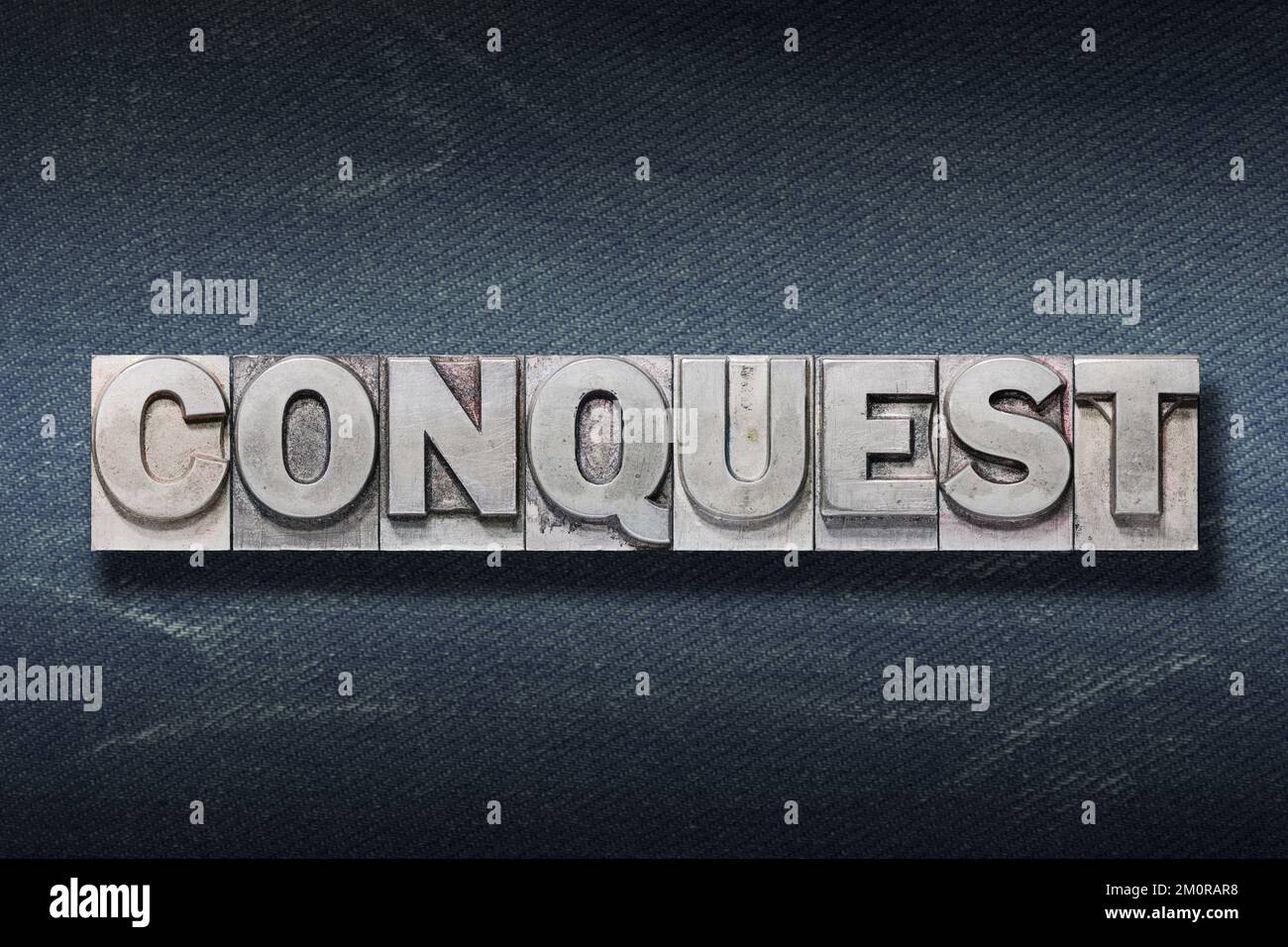 conquest word made from metallic letterpress on dark jeans background Stock Photo