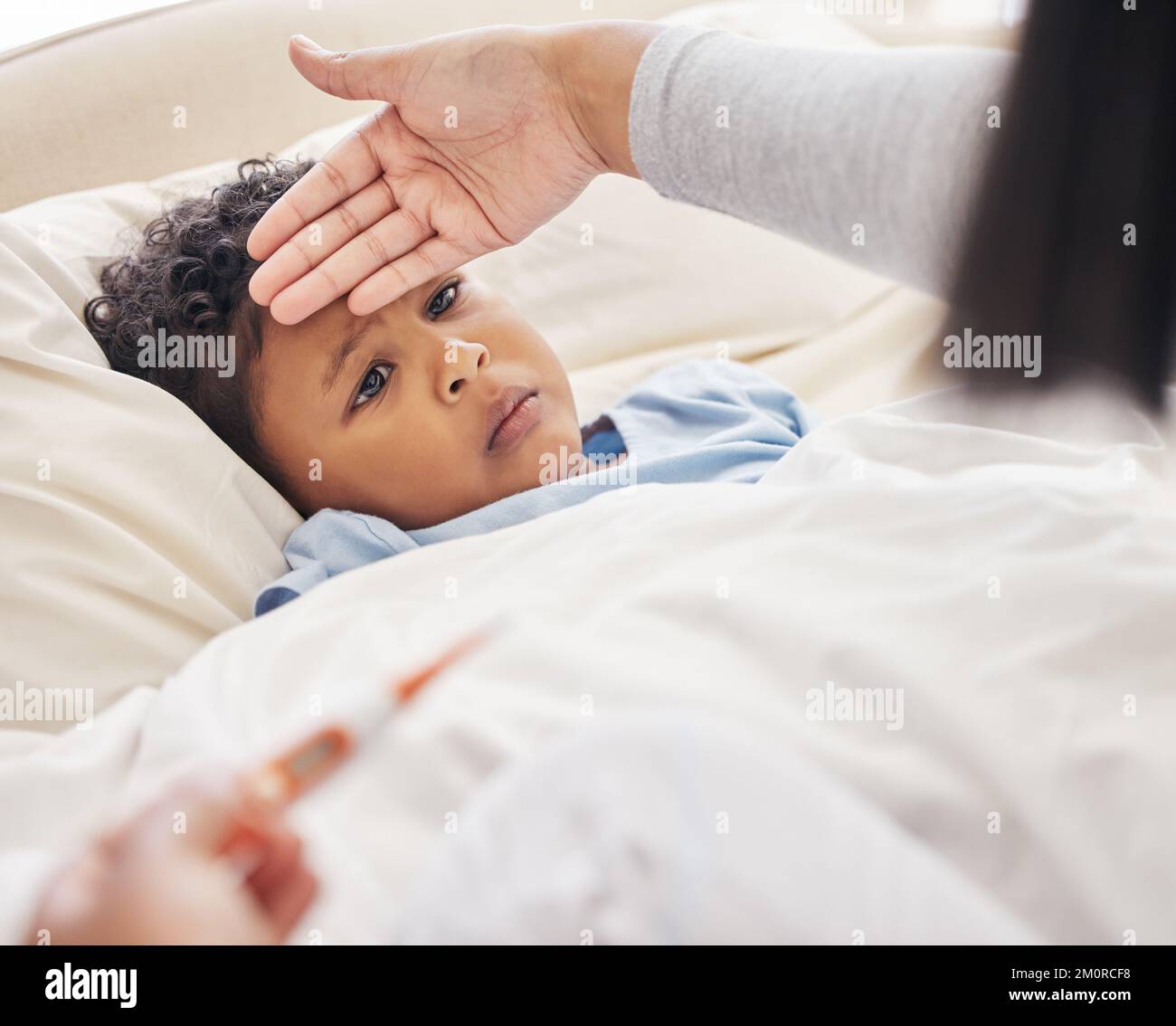 Sick little boy lying in bed while mother takes his temperature with