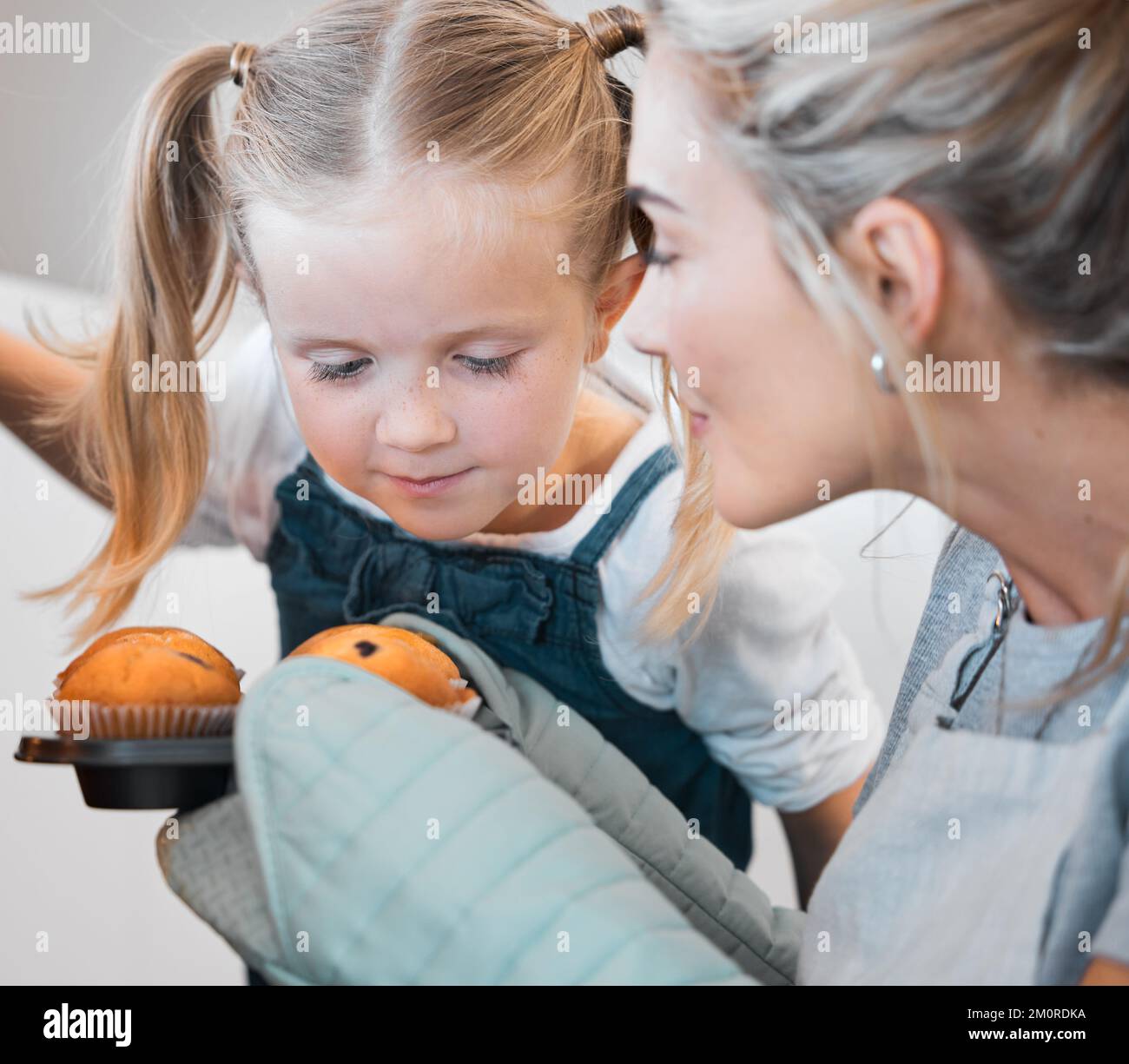 Mother and daughter smelling fresh, baked muffins. Young woman holding ...