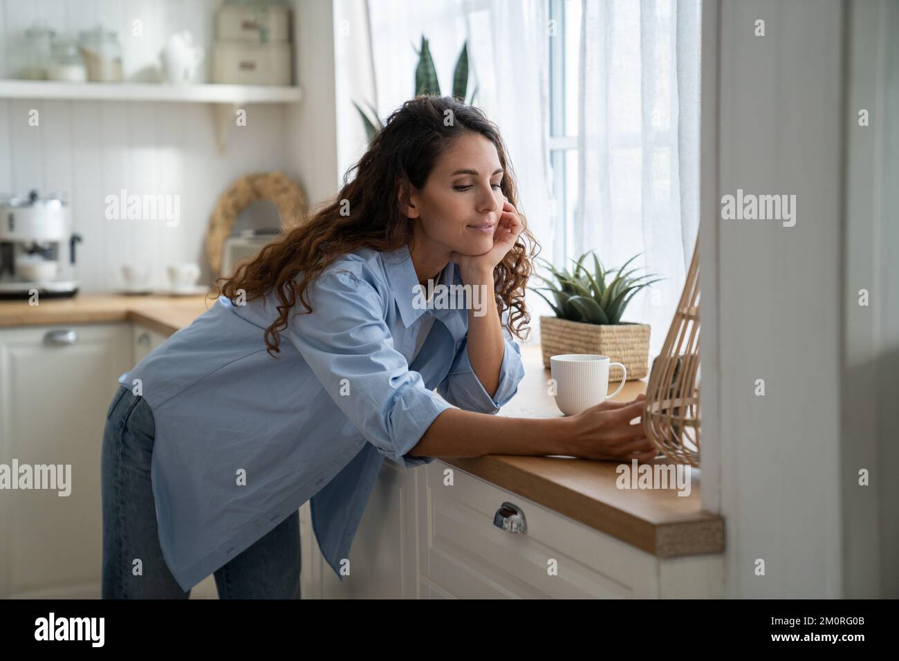 Smiling woman housewife standing in kitchen reading latest news on phone, ordering groceries online Stock Photo