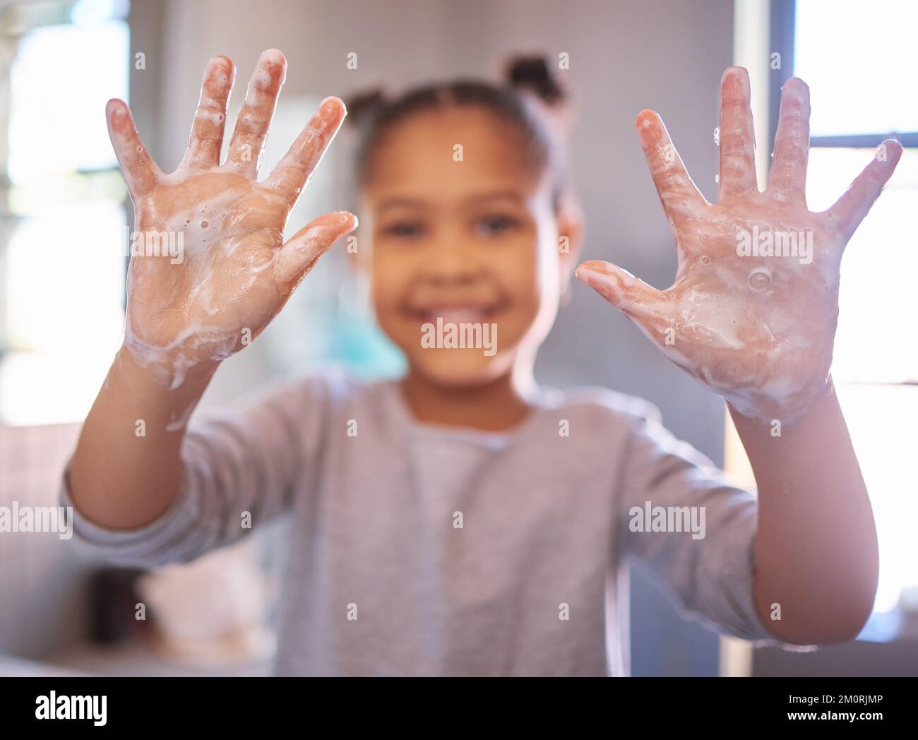 Little girl washing hands with water and soap in a bathroom. Happy kid showing soapy palms. Hand
