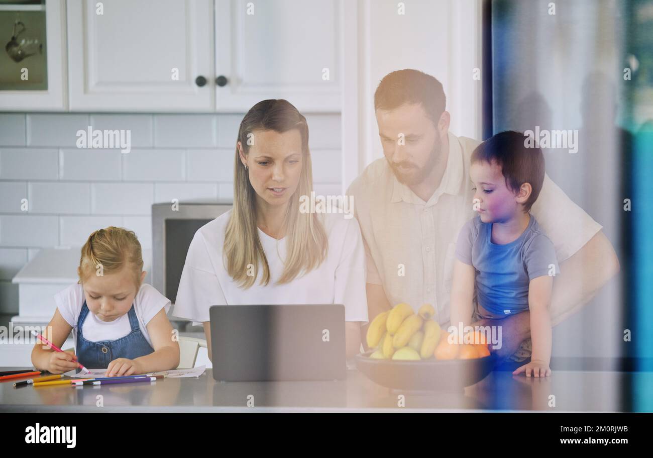 Caucasian family having lunch time with fresh fruit in a bright kitchen. Affectionate father helping his wife while shes using a laptop and sitting Stock Photo