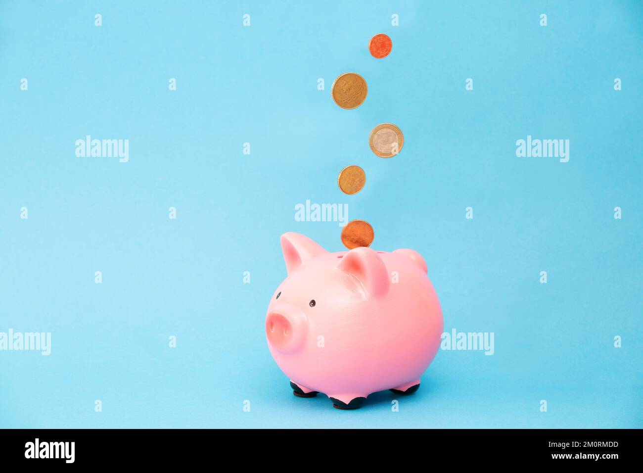 Coins falling into pink piggy bank on blue background. Concept savings ...