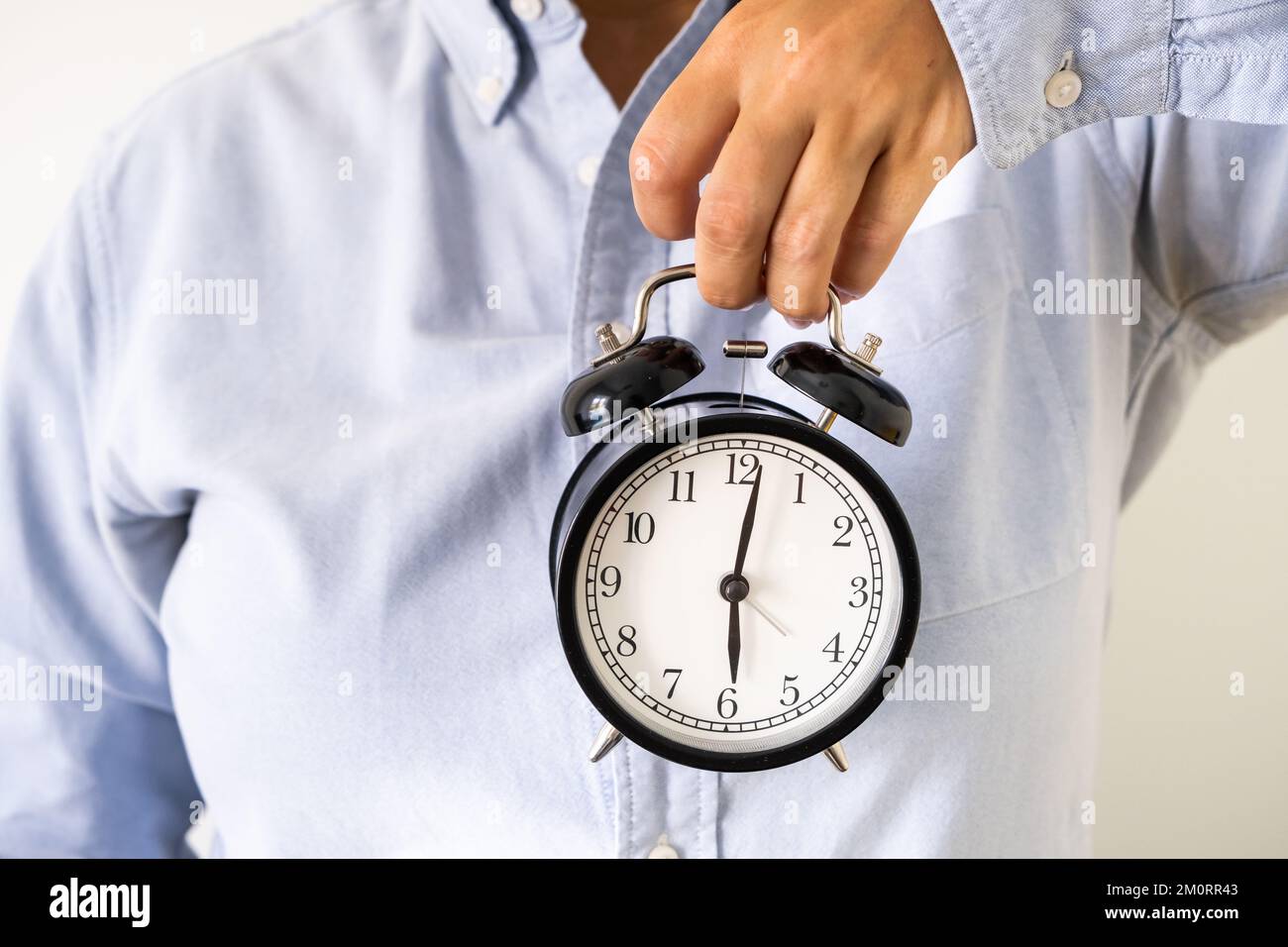 Woman's hand in office clothes holding an alarm clock at six o'clock in