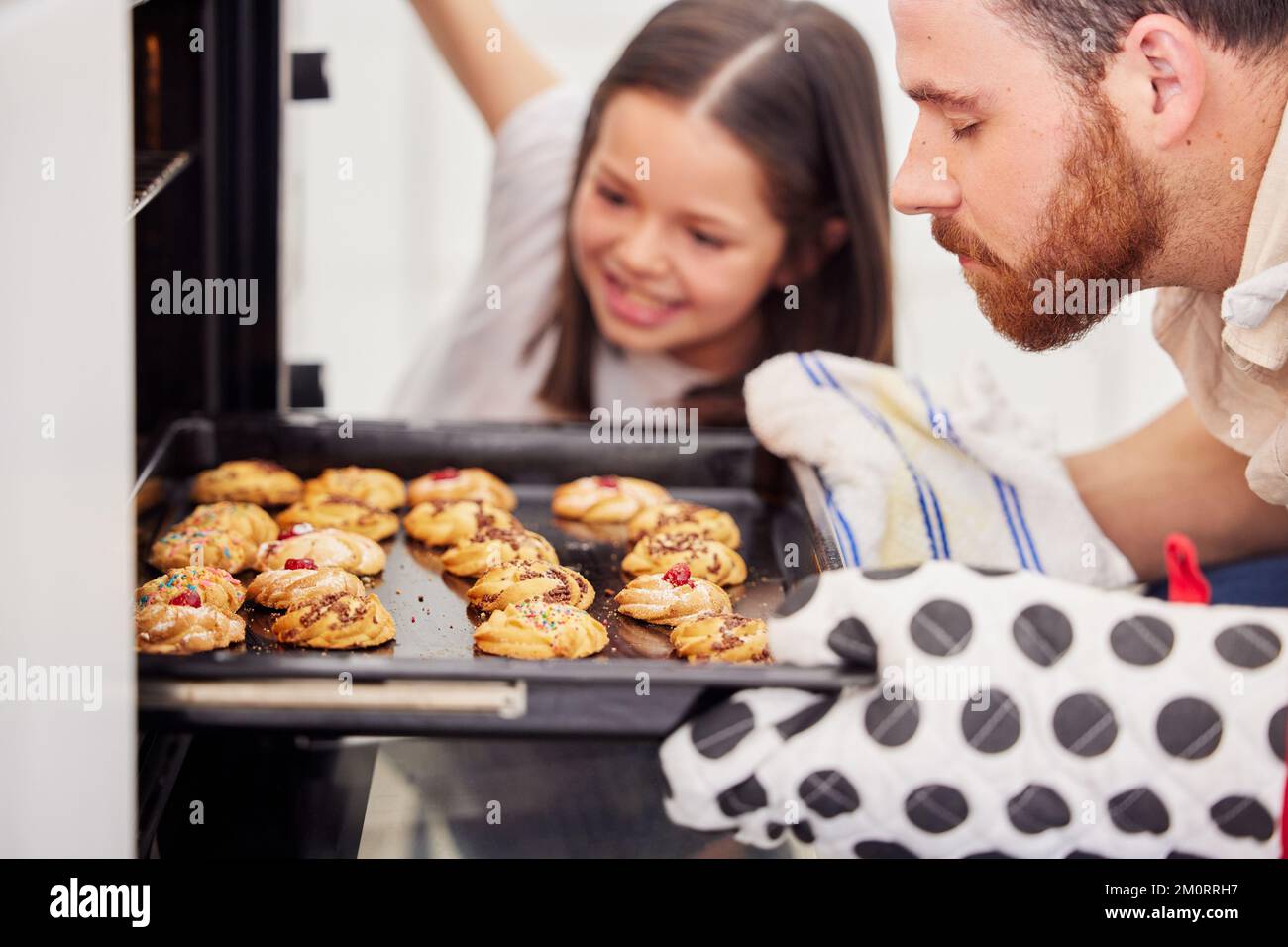 Father and daughter baking cookies at home. Parent taking baking tray with biscuits out the oven. Single dad and daughter preparing home bakery Stock Photo
