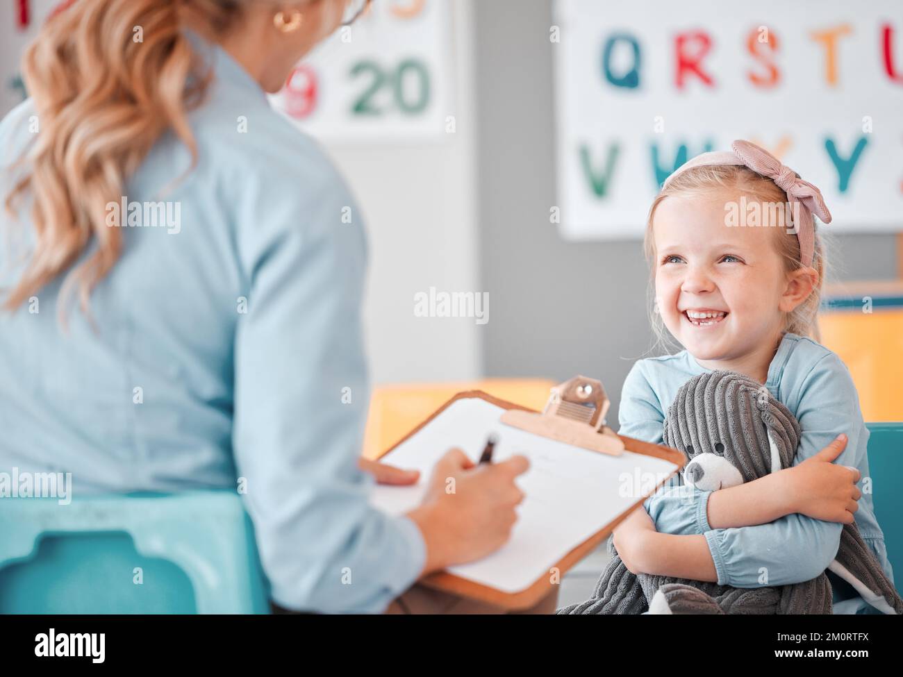 Smiling little girl with social worker in a clinic. Child psychologist writing on a clipboard during consult with adorable kid. Caucasian woman Stock Photo