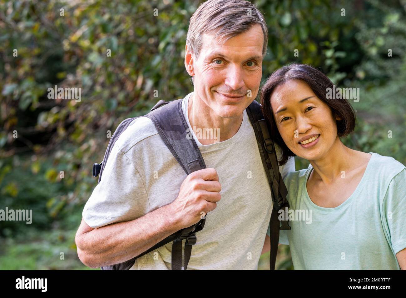 Middle-aged diverse couple looking at camera while hiking out in the woods Stock Photo