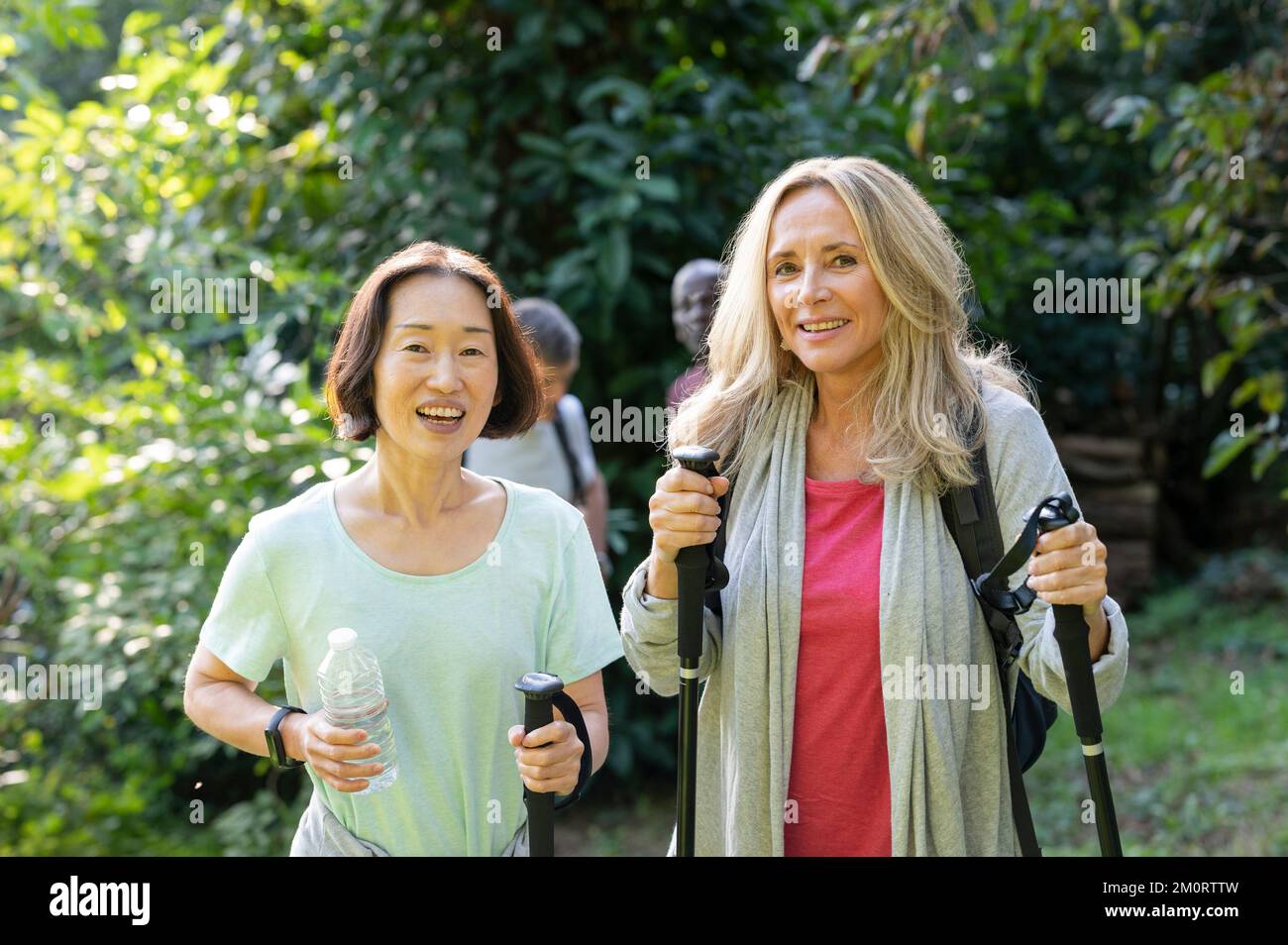 Two middle-aged ladies with hiking poles walking in the woods with their partners behind them Stock Photo