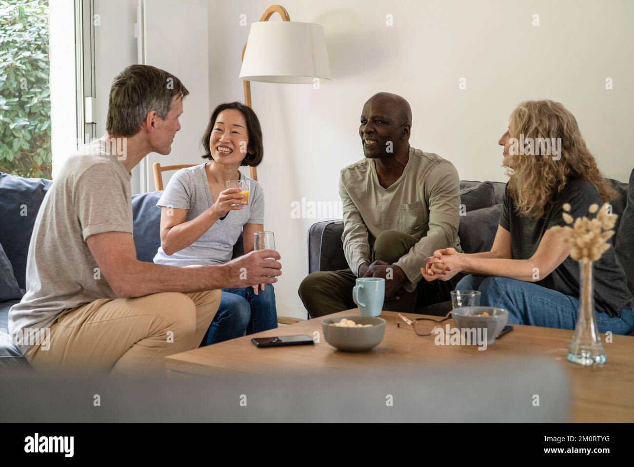 Group of senior friends sitting on sofa while drinking juice and tea Stock Photo