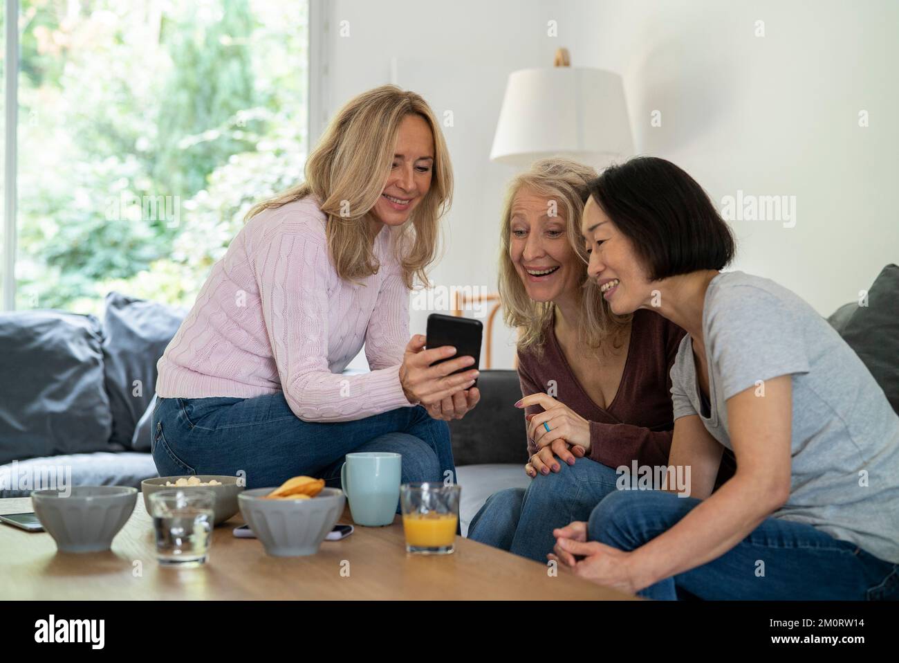Senior women watching video on smart phone while sitting on sofa Stock Photo