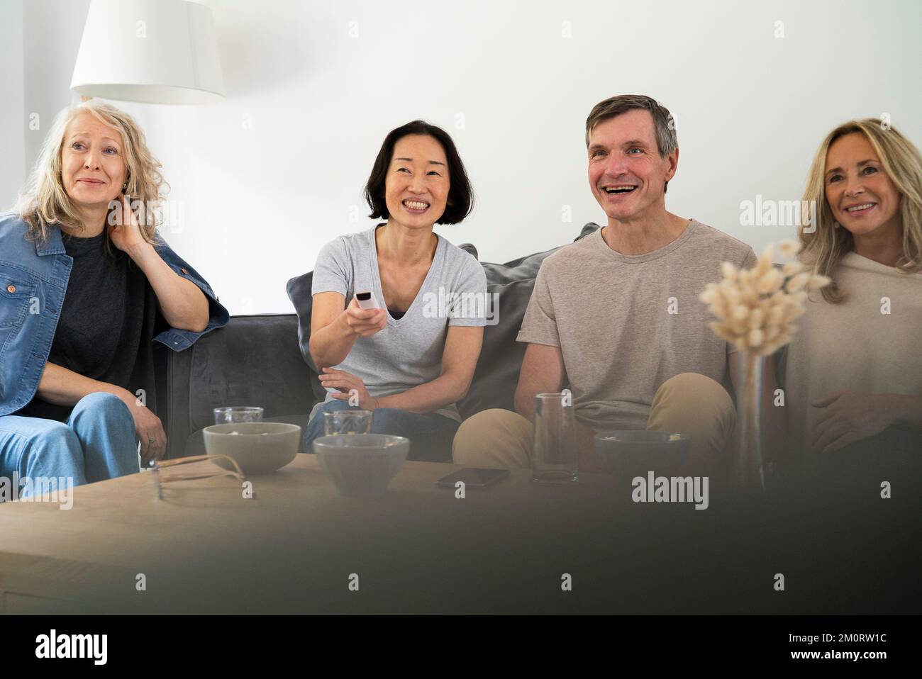 Diverse group of senior friends sitting on sofa watching TV Stock Photo