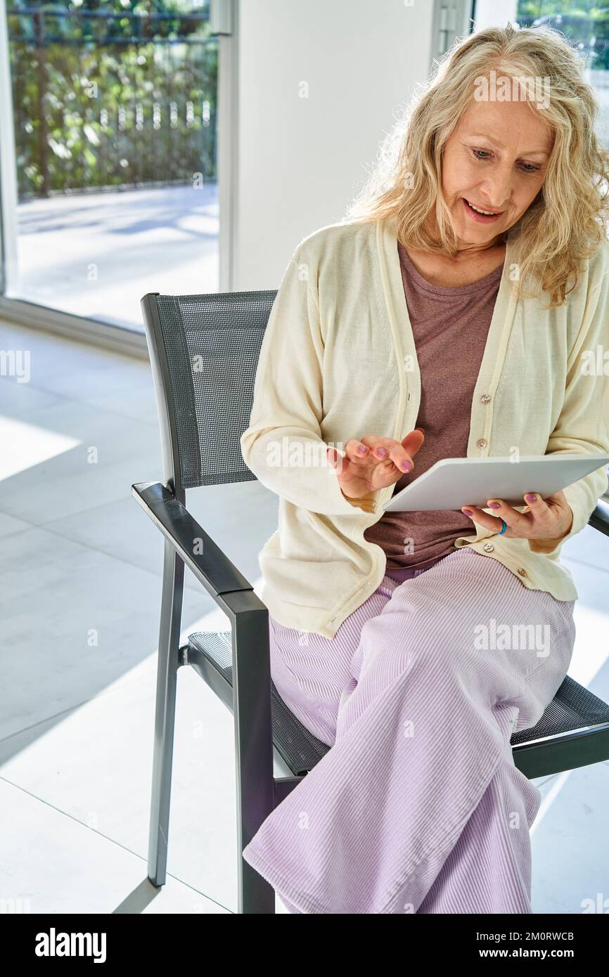 Senior woman using digital tablet while sitting on chair Stock Photo