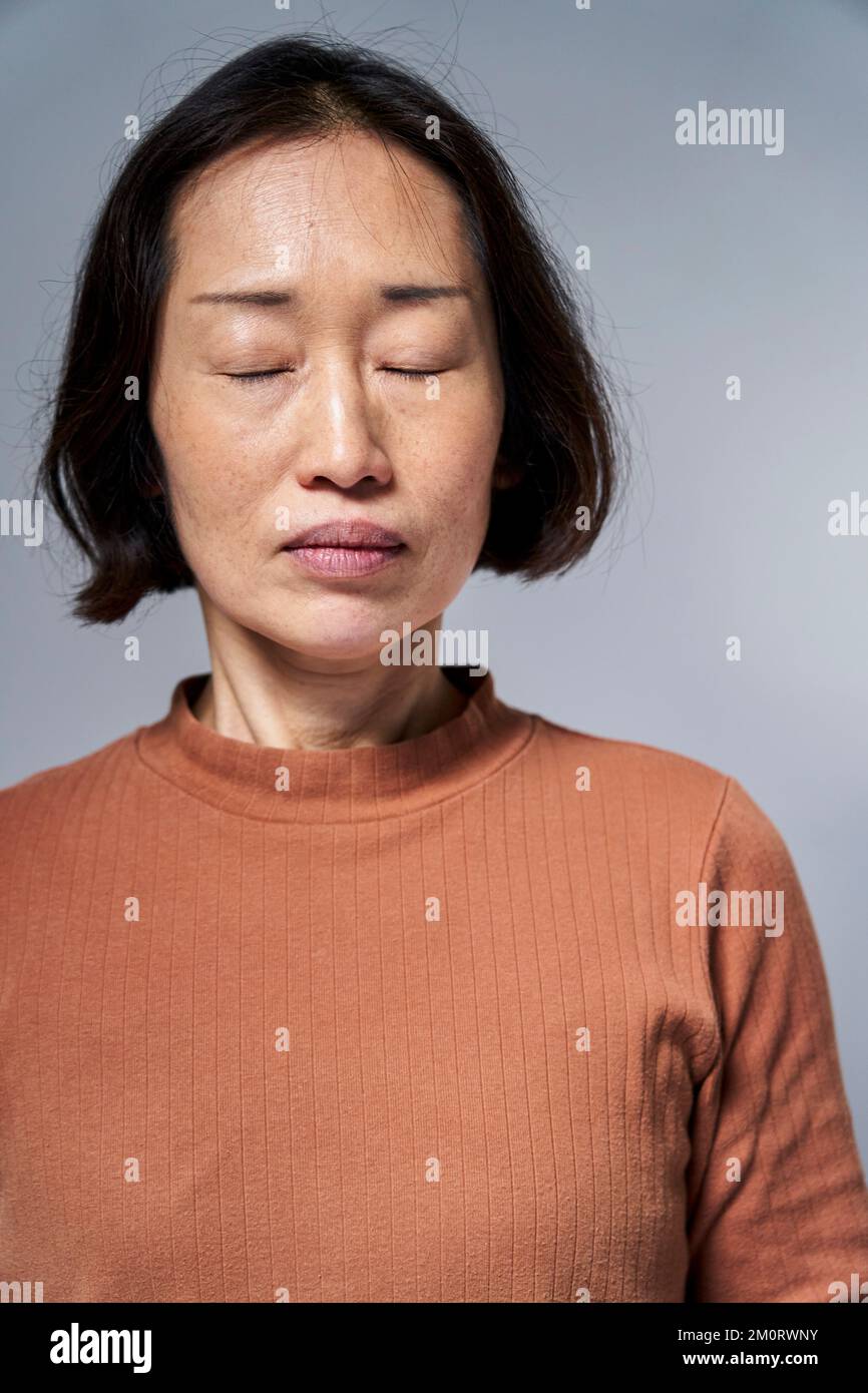 Mature Asian woman with eyes closed against white background Stock ...