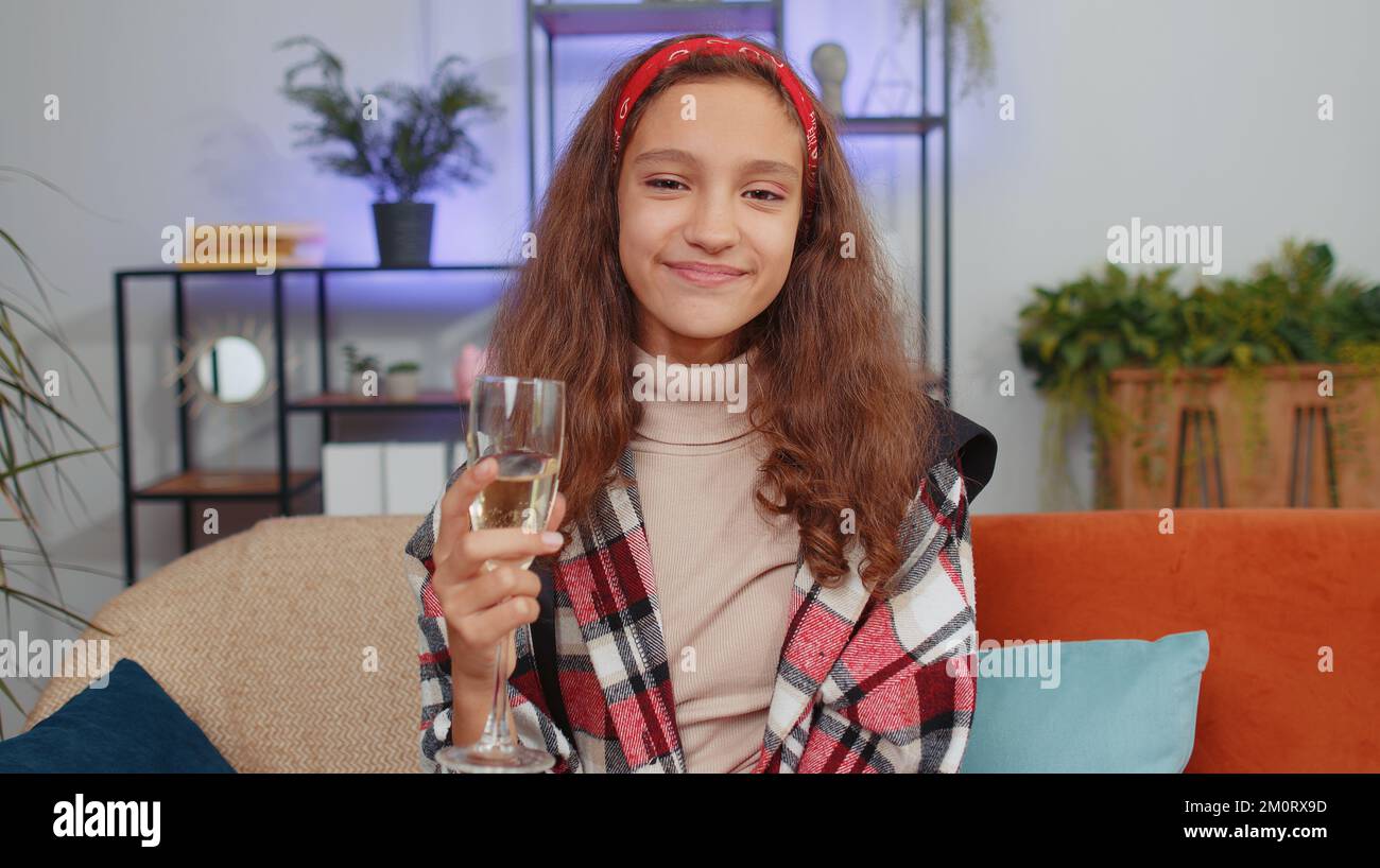 Joyful preteen girl child kid hold glass of champagne cheering and drinking, celebrate success win, career grow up, lucky situation at home. Teenager children celebrating rent or purchase of new house Stock Photo