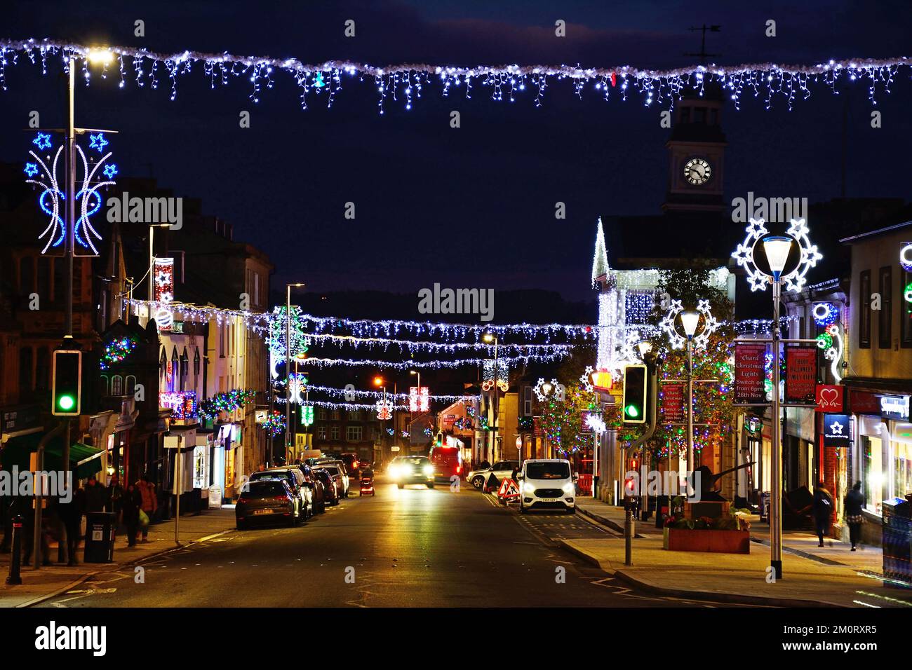View along the High Street and Fore Street with pretty Christmas decorations lit up at night, Chard, Somerset, UK, Europe. Stock Photo