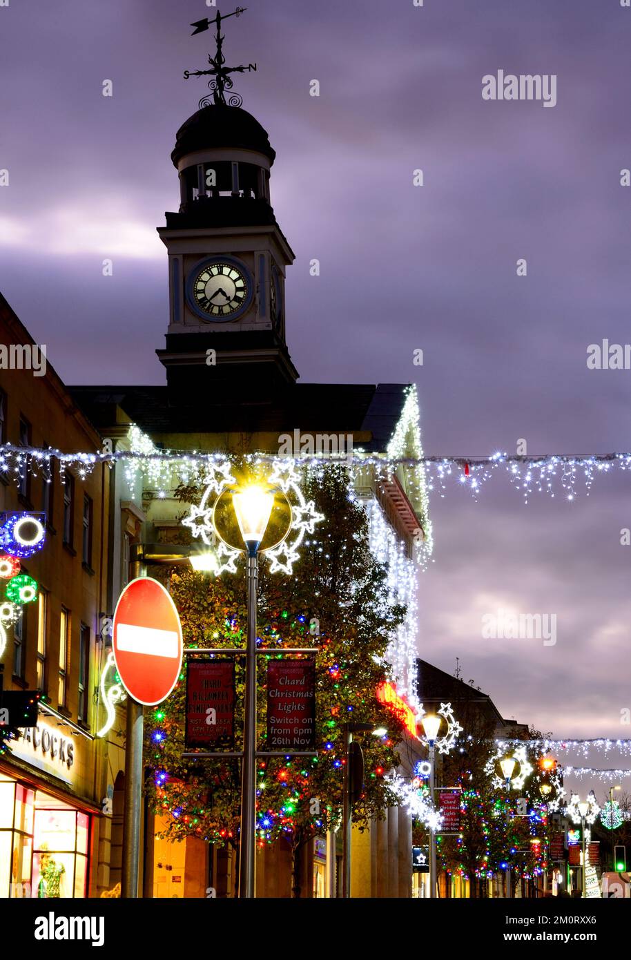 View along the High Street and Fore Street with pretty Christmas decorations lit up at night, Chard, Somerset, UK, Europe. Stock Photo