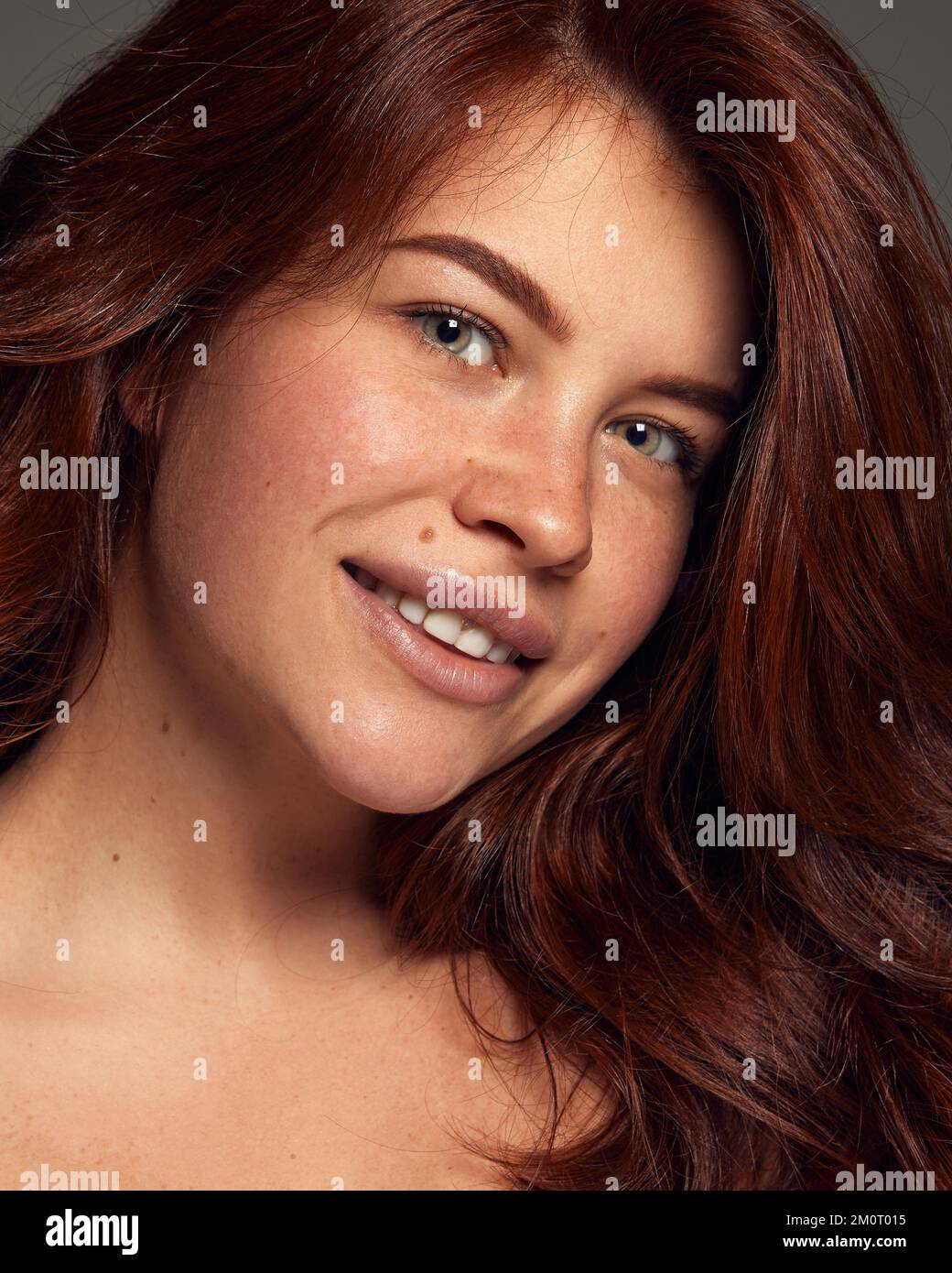 Portrait of young beautiful red-haired woman with perfect natural skin with freckles isolated on dark grey background. Glossy wavy hair Stock Photo