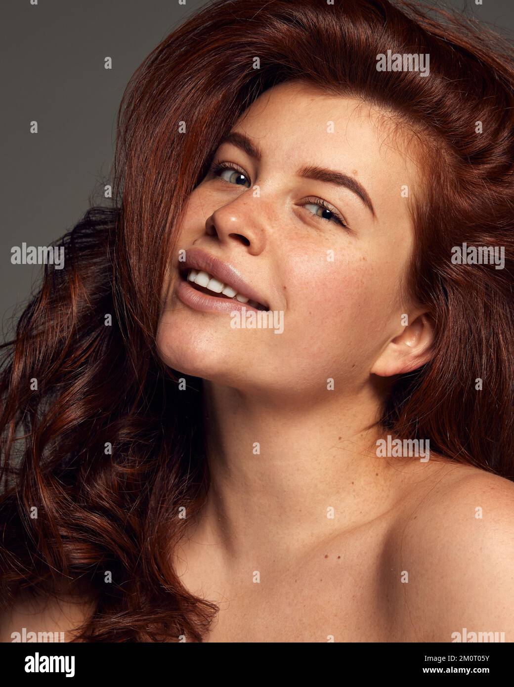 Portrait of young beautiful red-haired woman with perfect skin with freckles isolated on dark grey background. Hair dying, treatment Stock Photo