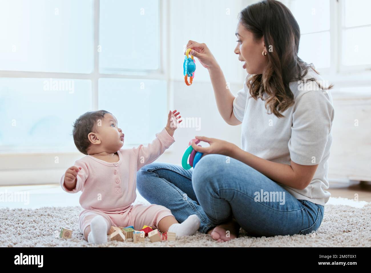 Give me that. a young mother bonding with her baby while sitting on the floor at home. Stock Photo
