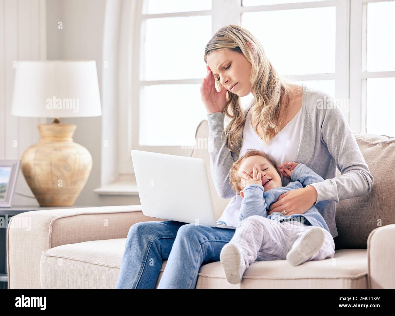 I cant work like this. a woman looking stressed while working on her laptop and sitting with her crying baby. Stock Photo
