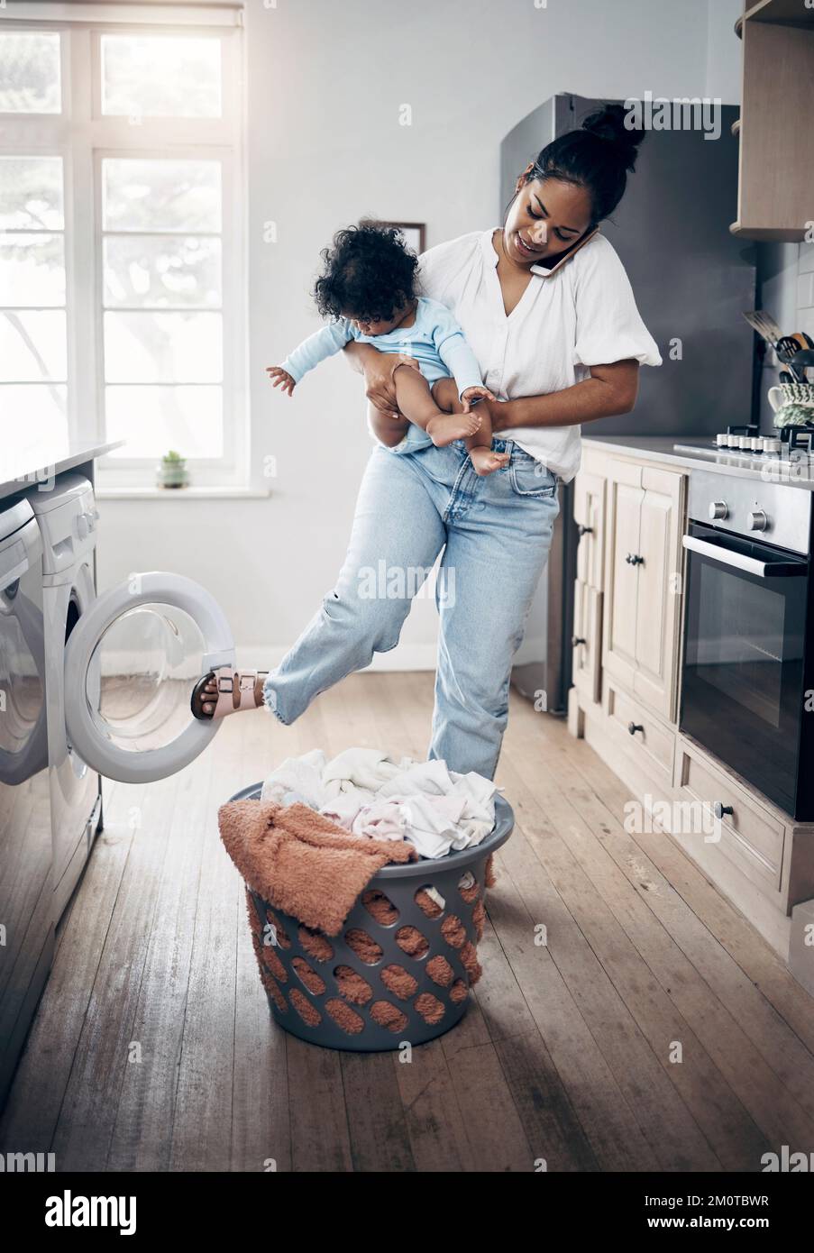 Babys laundry cannot wait. a young mother using a cellphone while completing housework and holding her baby at home. Stock Photo