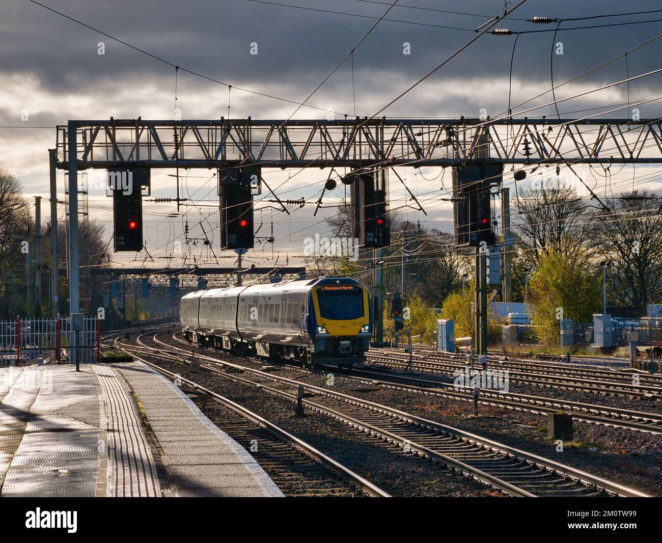 A commuter train arrives at Preston station in the north of the UK. Overhead signals and power lines are visible. Stock Photo