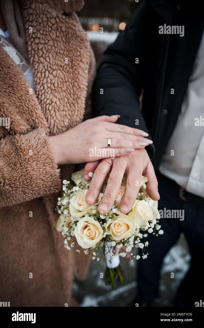 Hands of the newlyweds with wedding rings on the wedding bouquet. Hands of the bride and groom on a bouquet of flowers. Stock Photo