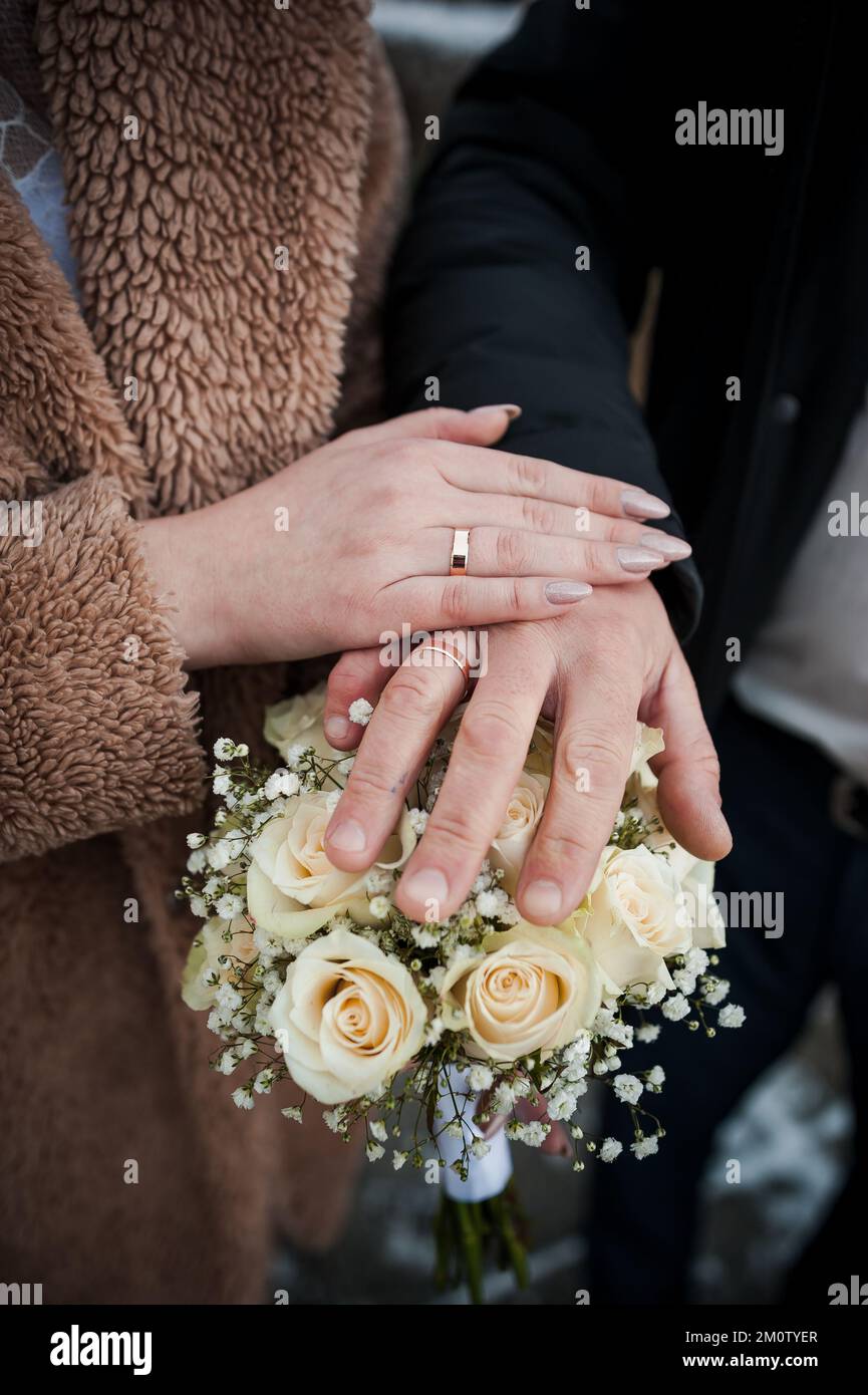 Hands of the newlyweds with wedding rings on the wedding bouquet. Hands of the bride and groom on a bouquet of flowers. Stock Photo