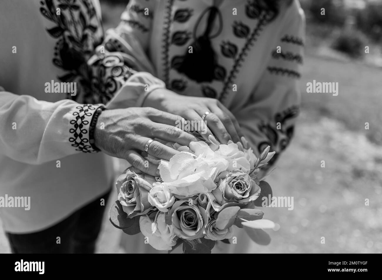 Hands of the newlyweds with wedding rings on the wedding bouquet. Hands of the bride and groom on a bouquet of flowers. Stock Photo