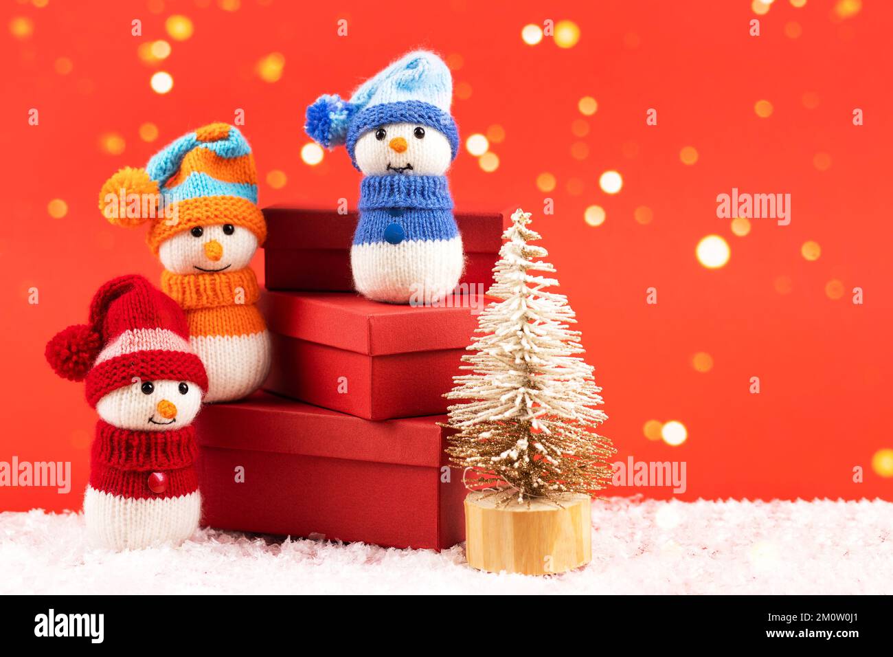 Knitted snowmen in a red hat and sweater stands on three red gift boxes ...