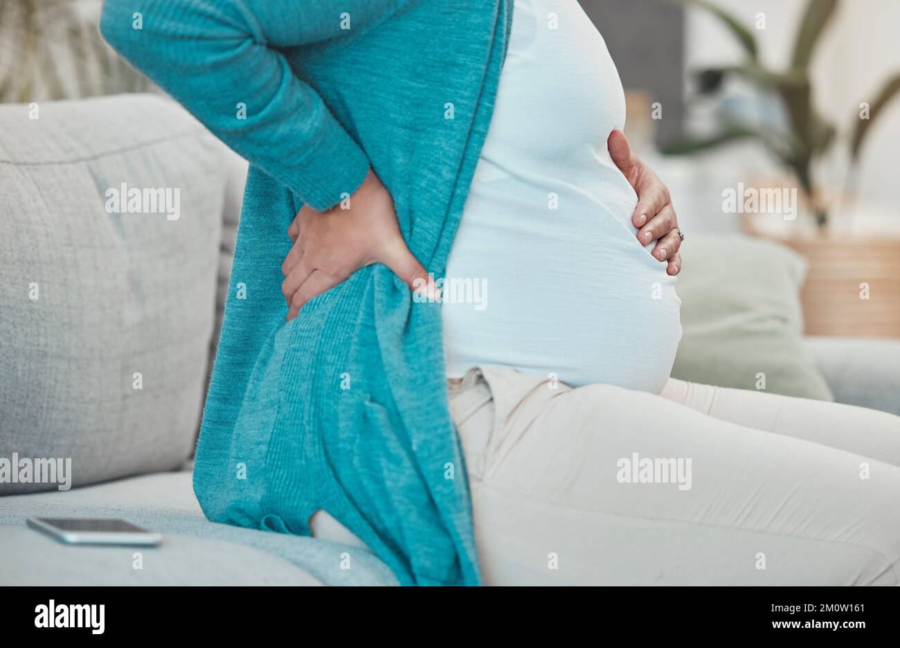 Back pain, pregnancy and woman relaxing on a sofa in her living room at her modern house