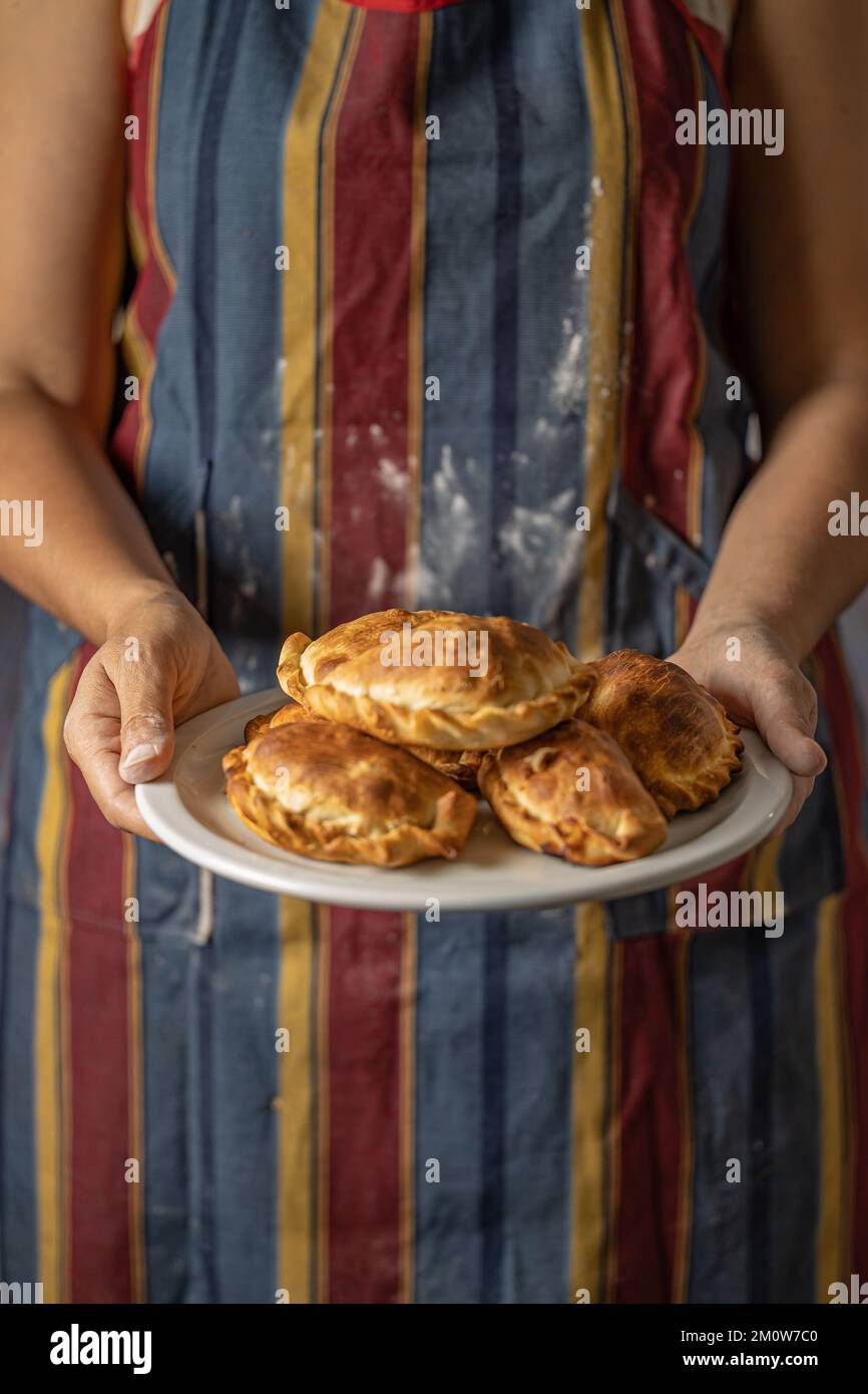 Woman in an apron stained with flour holding a tray with Argentine empanadas with copy space. Stock Photo