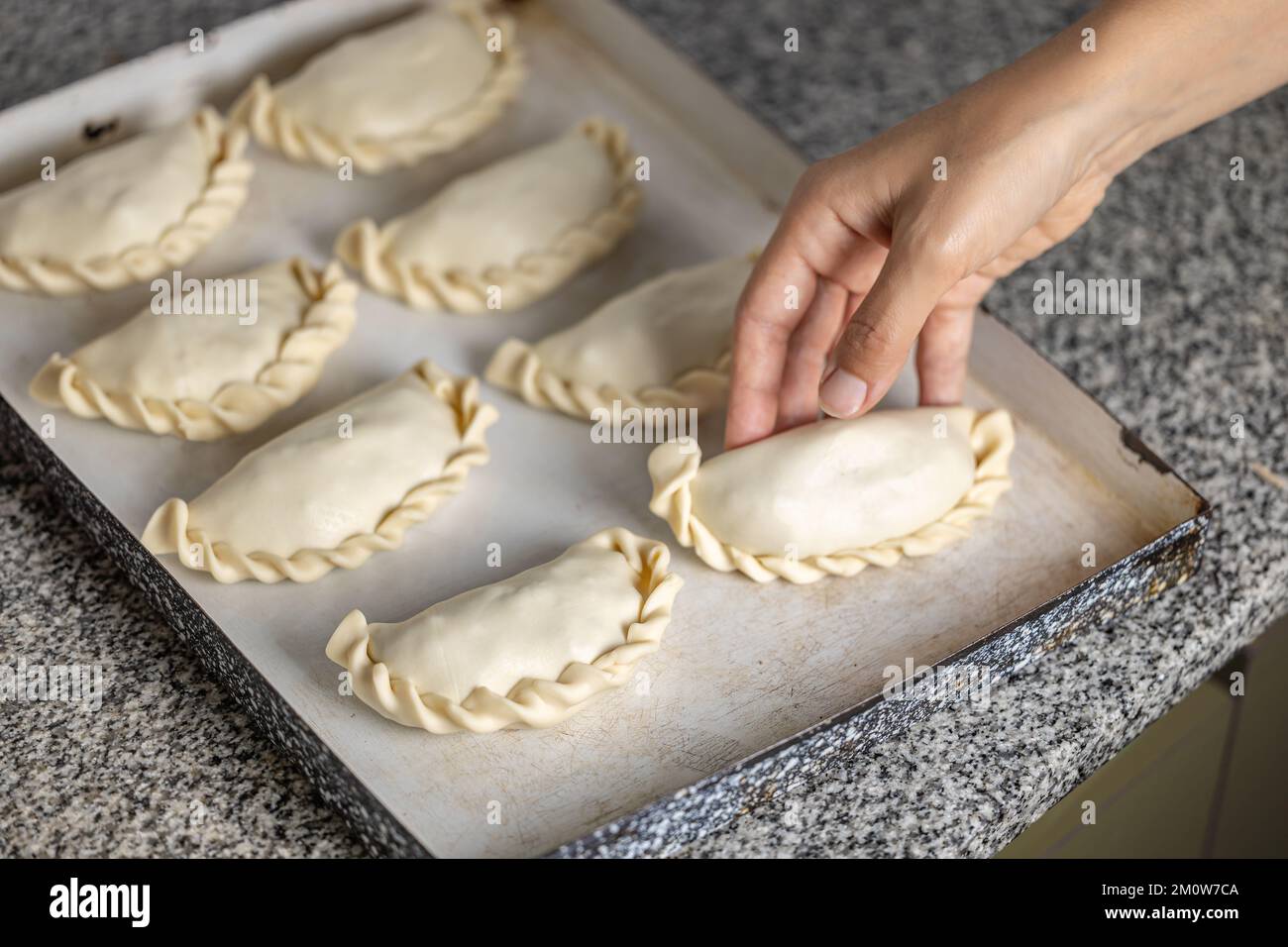 Woman's hands putting Argentine empanadas on a platter. Stock Photo