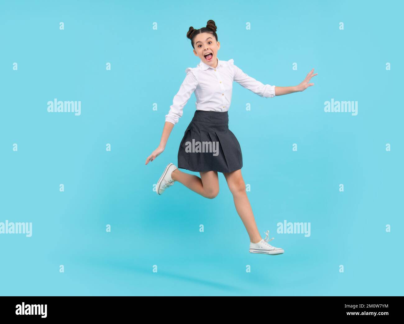 Happy funny jumping teenager. Happy schoolgirl, positive and smiling emotions of teen girl. Full length jump of teenager girl on blue isolated studio Stock Photo