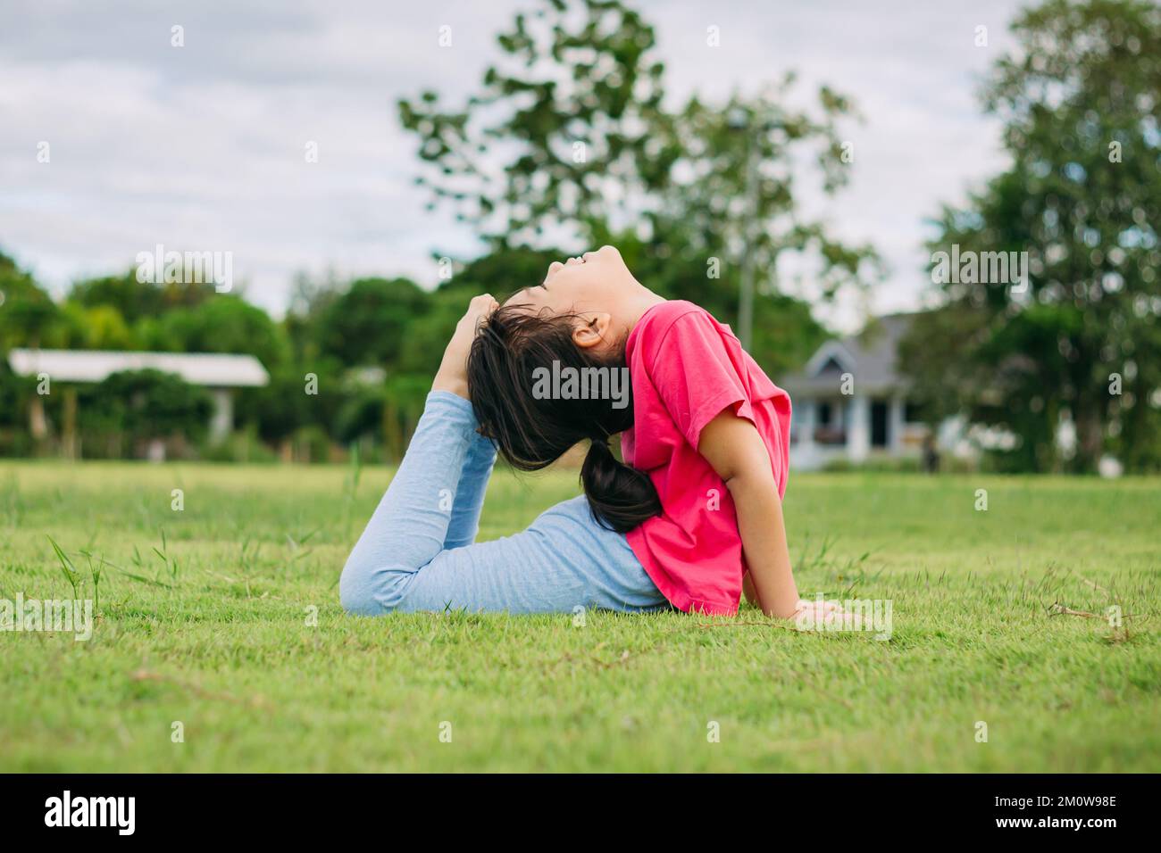 Children meditation with yoga pose on green grass field. Outdoors activity for kids to practicing yoga, children can learn how to exercise. Stock Photo