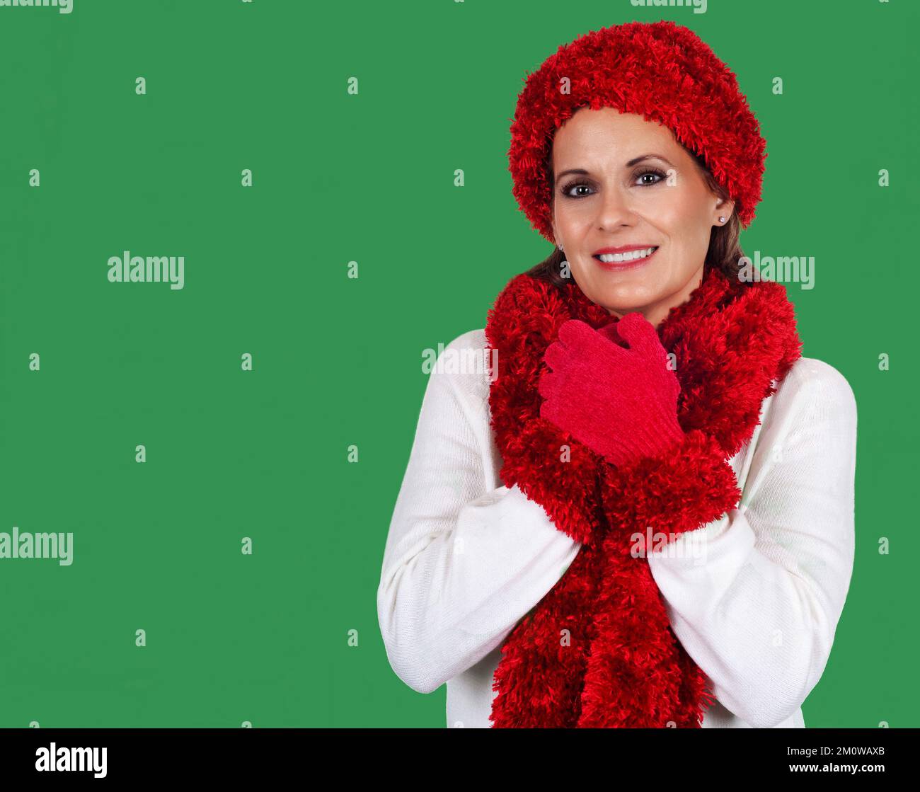 Beautiful Mature Woman wearing White Sweater with Red Hat, Scarf and Gloves against a Green Background for the Holiday Season Stock Photo