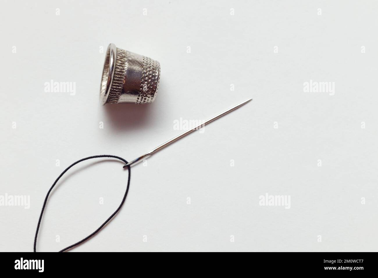 Sewing tools on white fabric background.Needle, thread, thimble and button. Horizontal composition. Top view Stock Photo