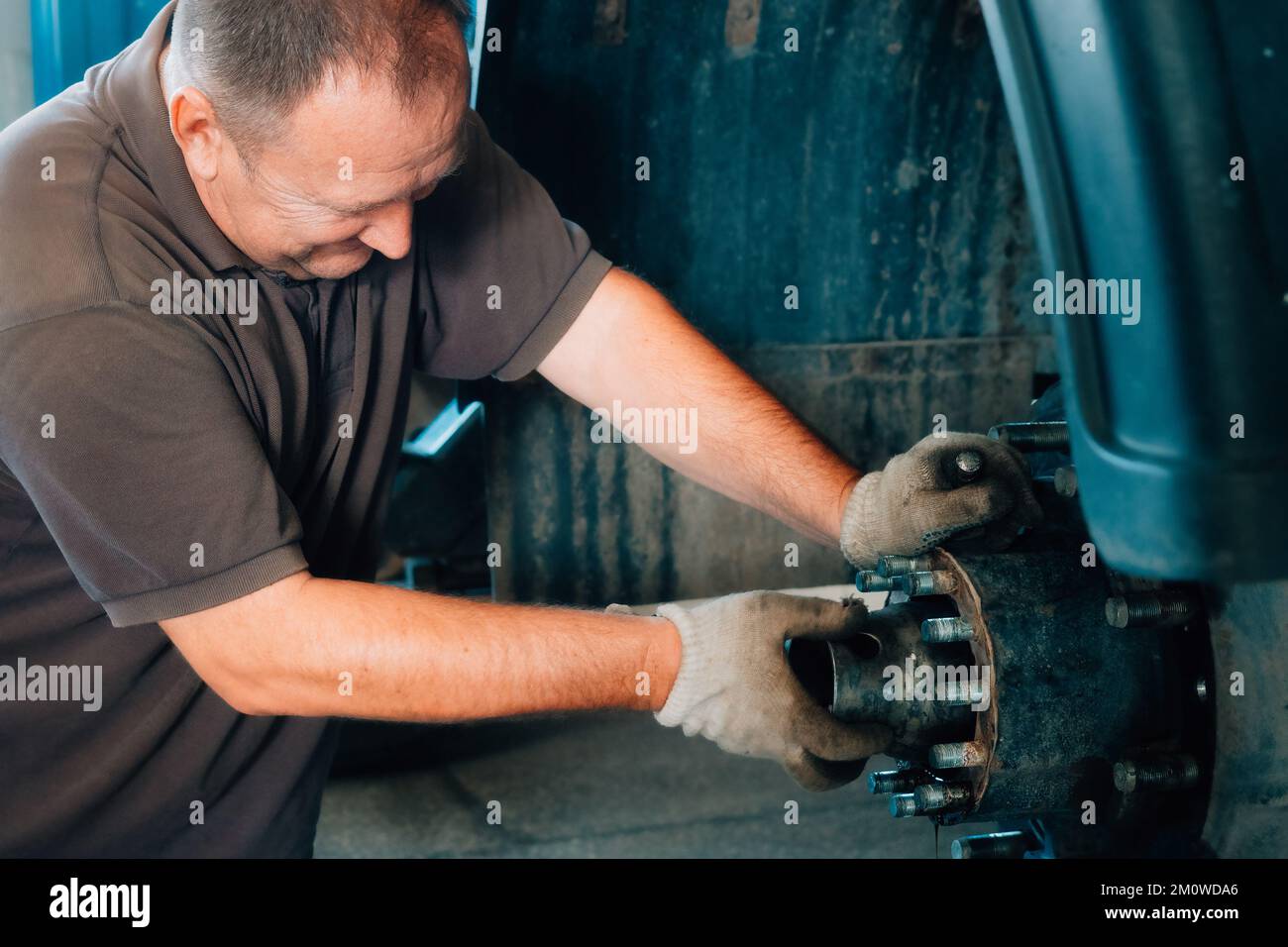 Auto mechanic repairs hub of truck in car repair shop. White Caucasian man in gloves disassembles car. Service for repair of large trucks and tractors. Background. Real workflow.. Stock Photo