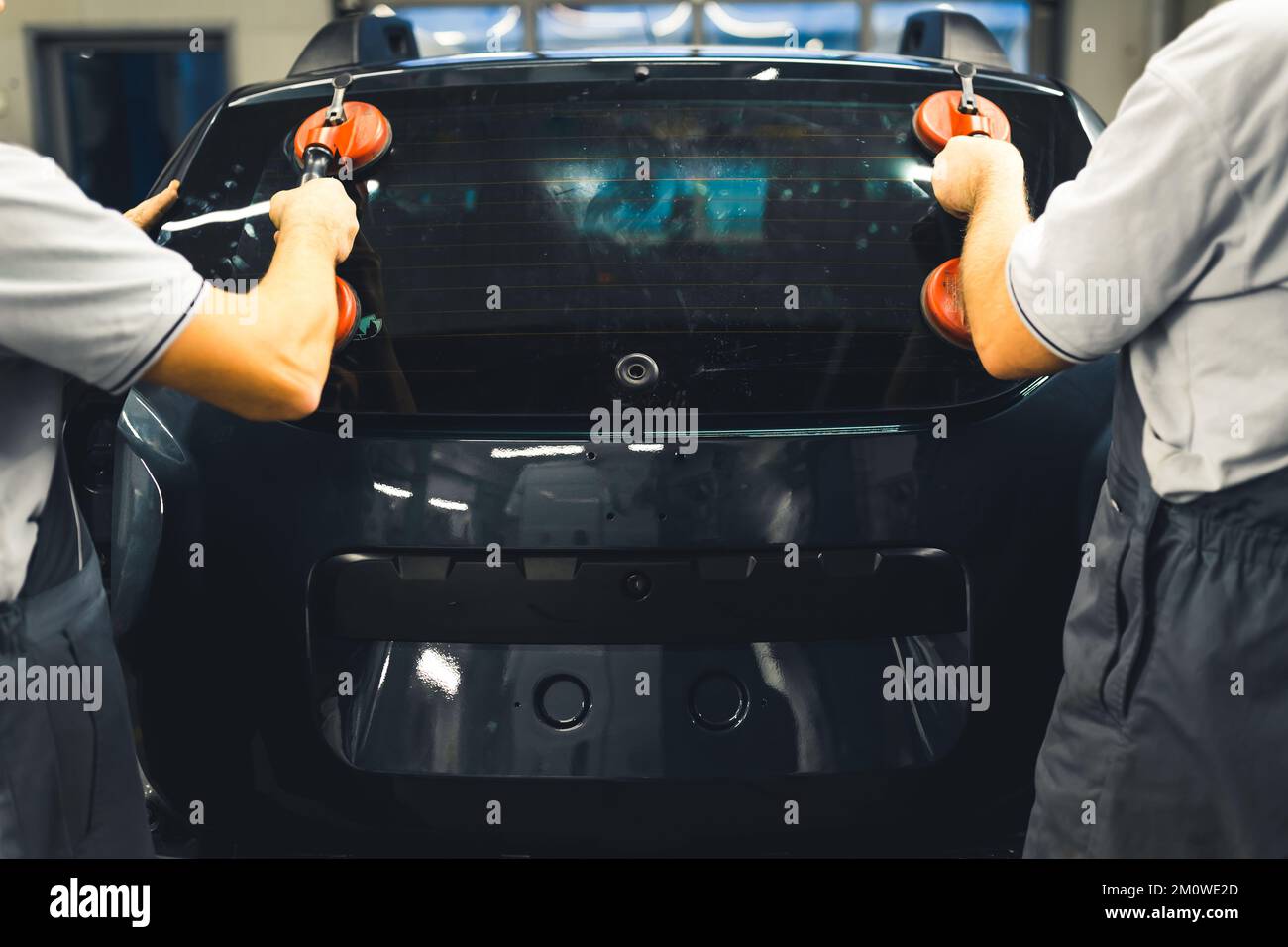 Back indoor view of two mechanics in gray uniforms using suction cups